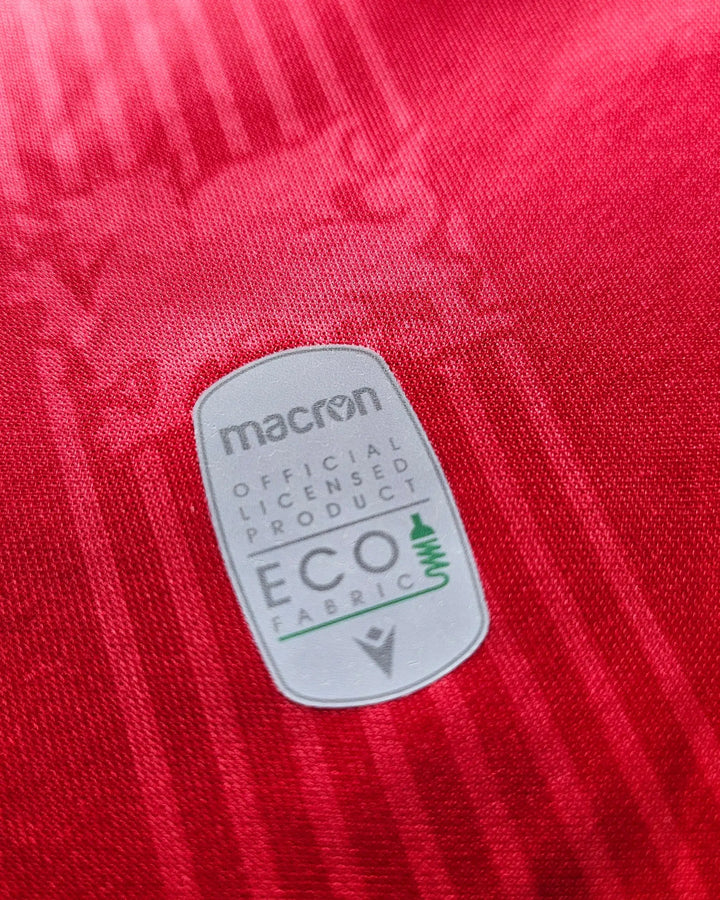 Detail showing the eco fabric label with macron branding on a red Wrexham AFC jersey.