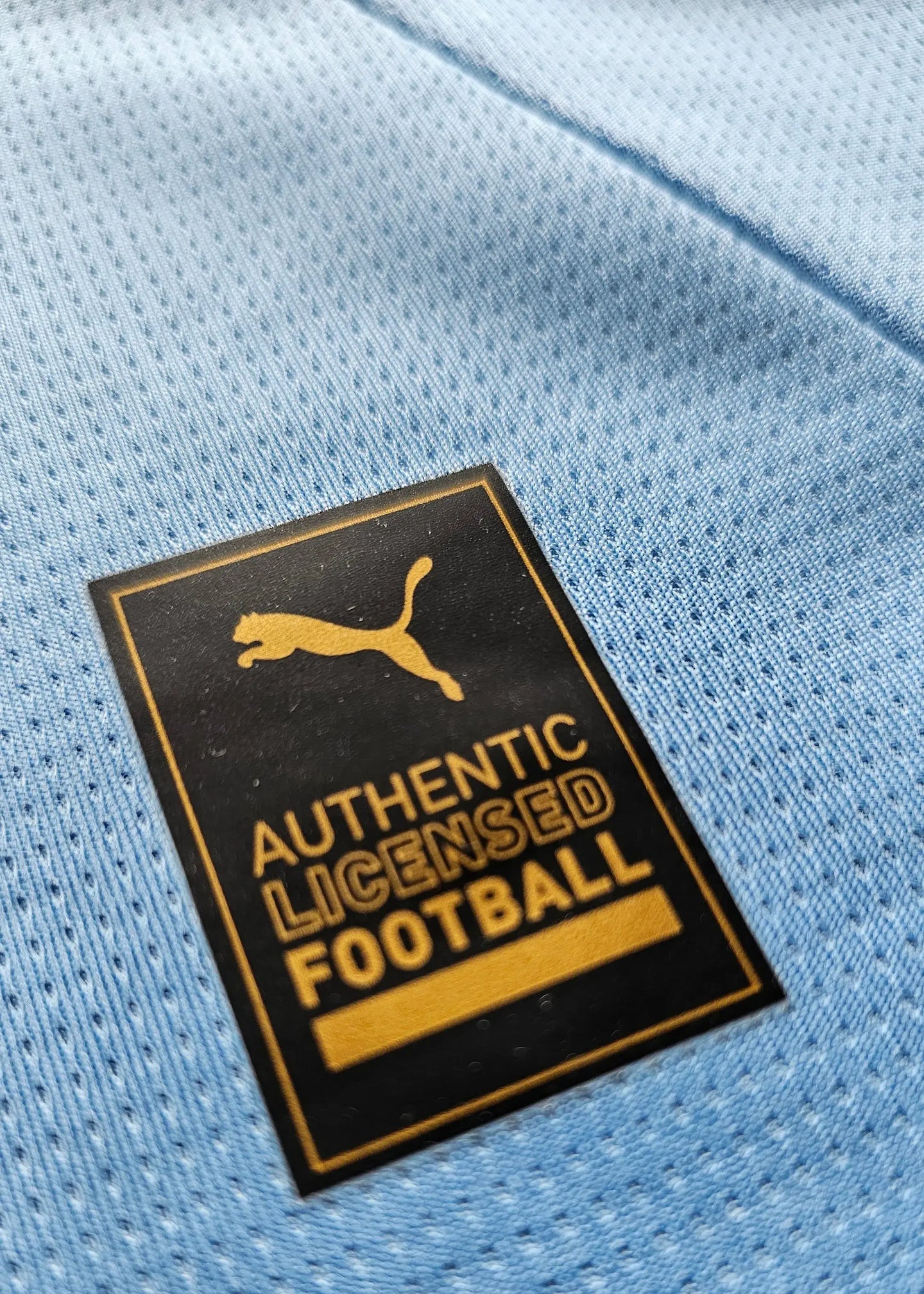 Close-up of the Puma Authentic Licensed Football tag on a light blue fabric.