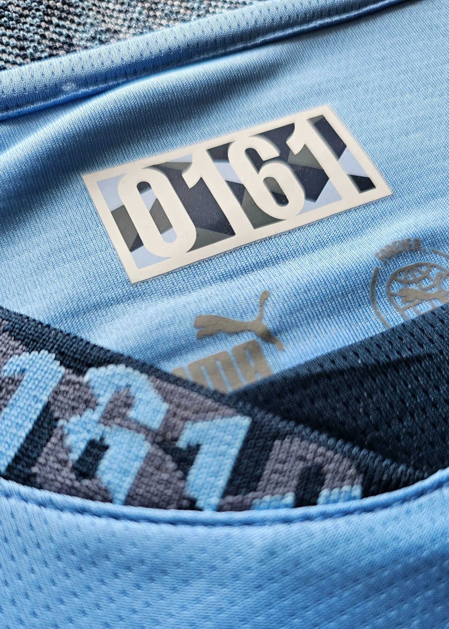 Crest detail showing Manchester City badge and 0161 under collar with Puma logo.