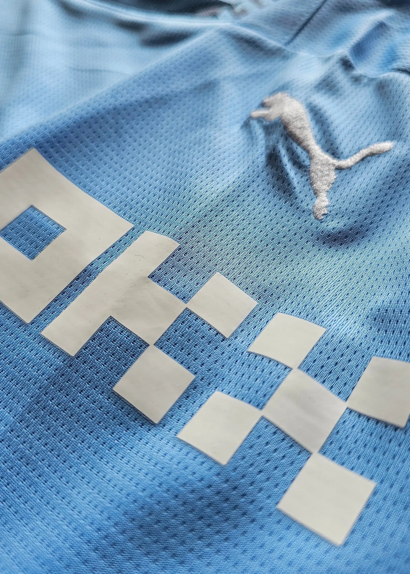 Detail showing woven blue fabric with Puma logo and sponsor text on the signed football shirt.