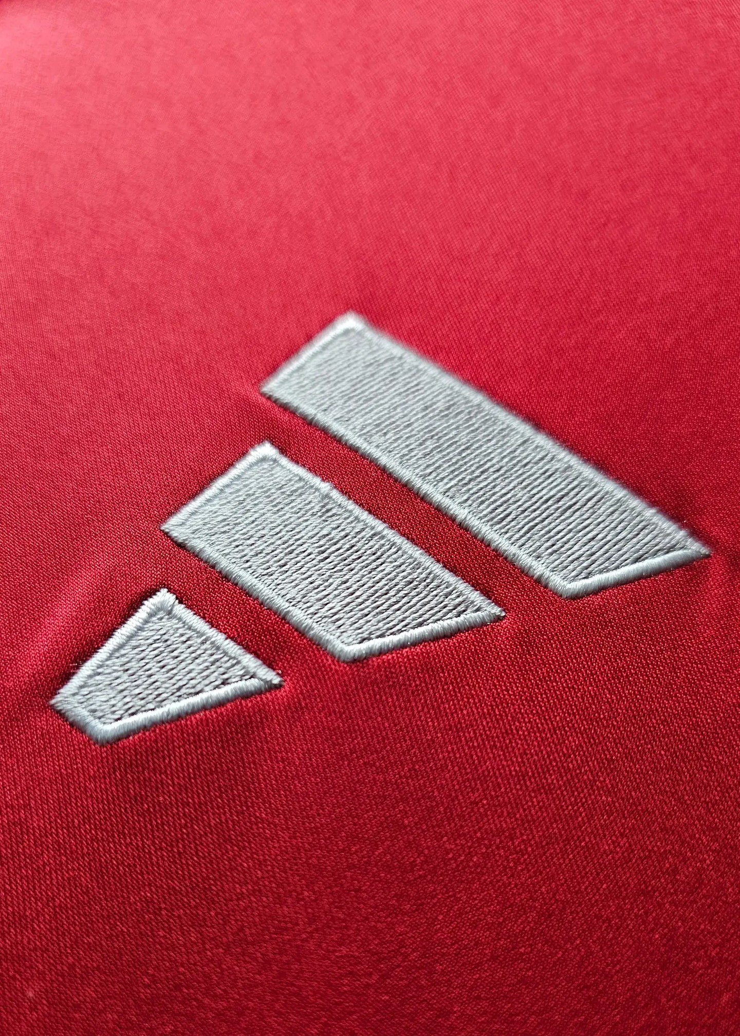 Close-up of the adidas logo on a red fabric background.