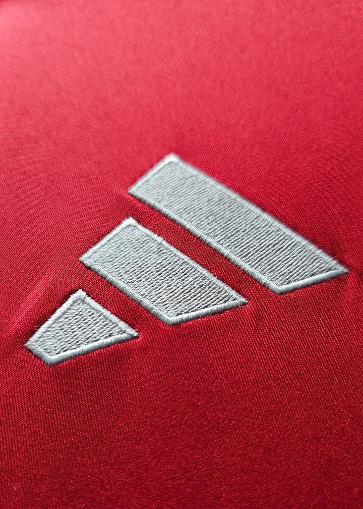 Close-up of the adidas logo on a red fabric background.
