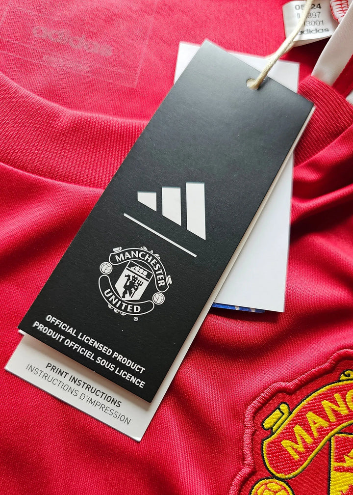 Detailed view showing Manchester United crest, adidas tag, and care instructions on red football shirt.
