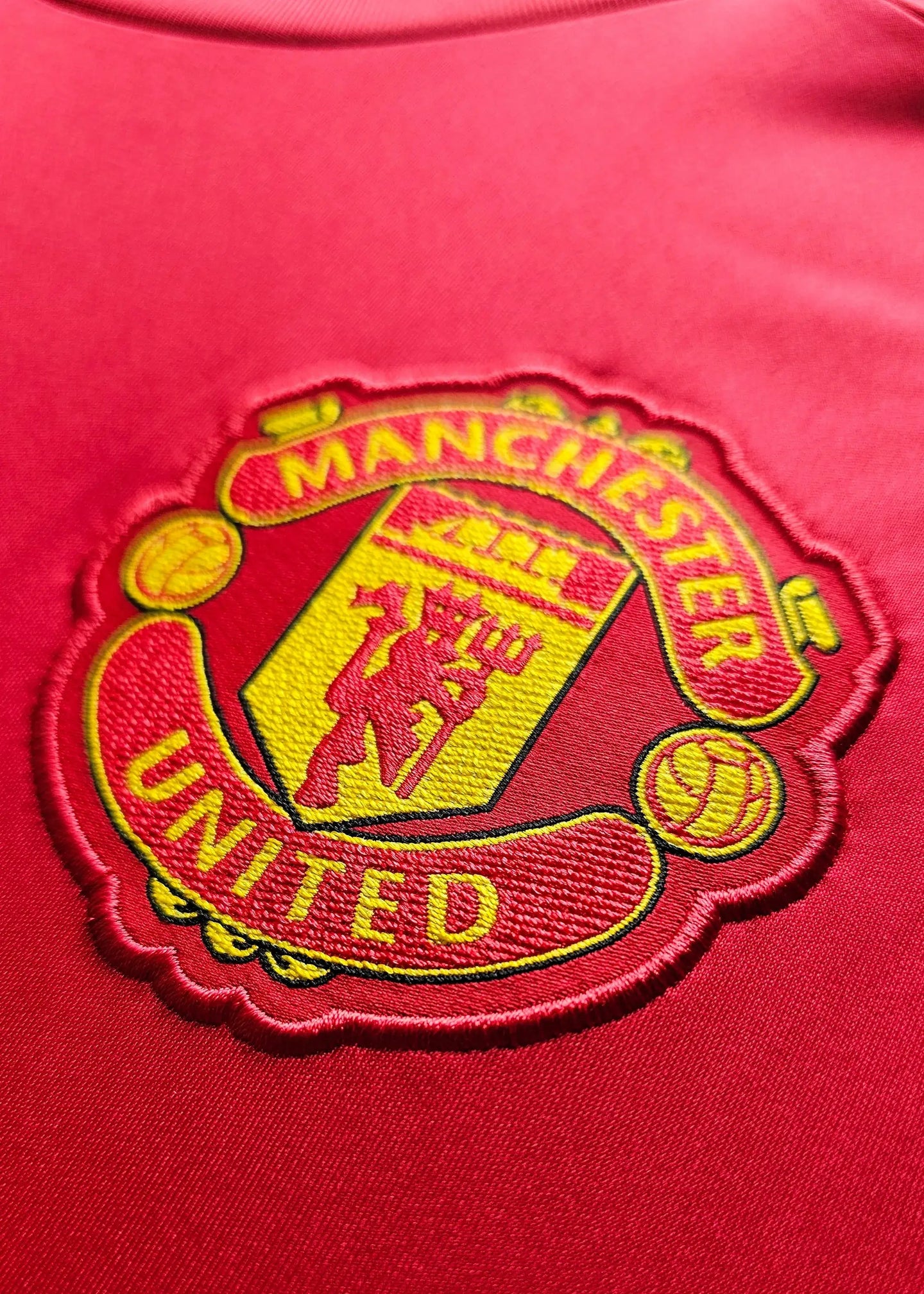 Close-up of Manchester United crest in red and yellow with 'MANCHESTER' and 'UNITED'.