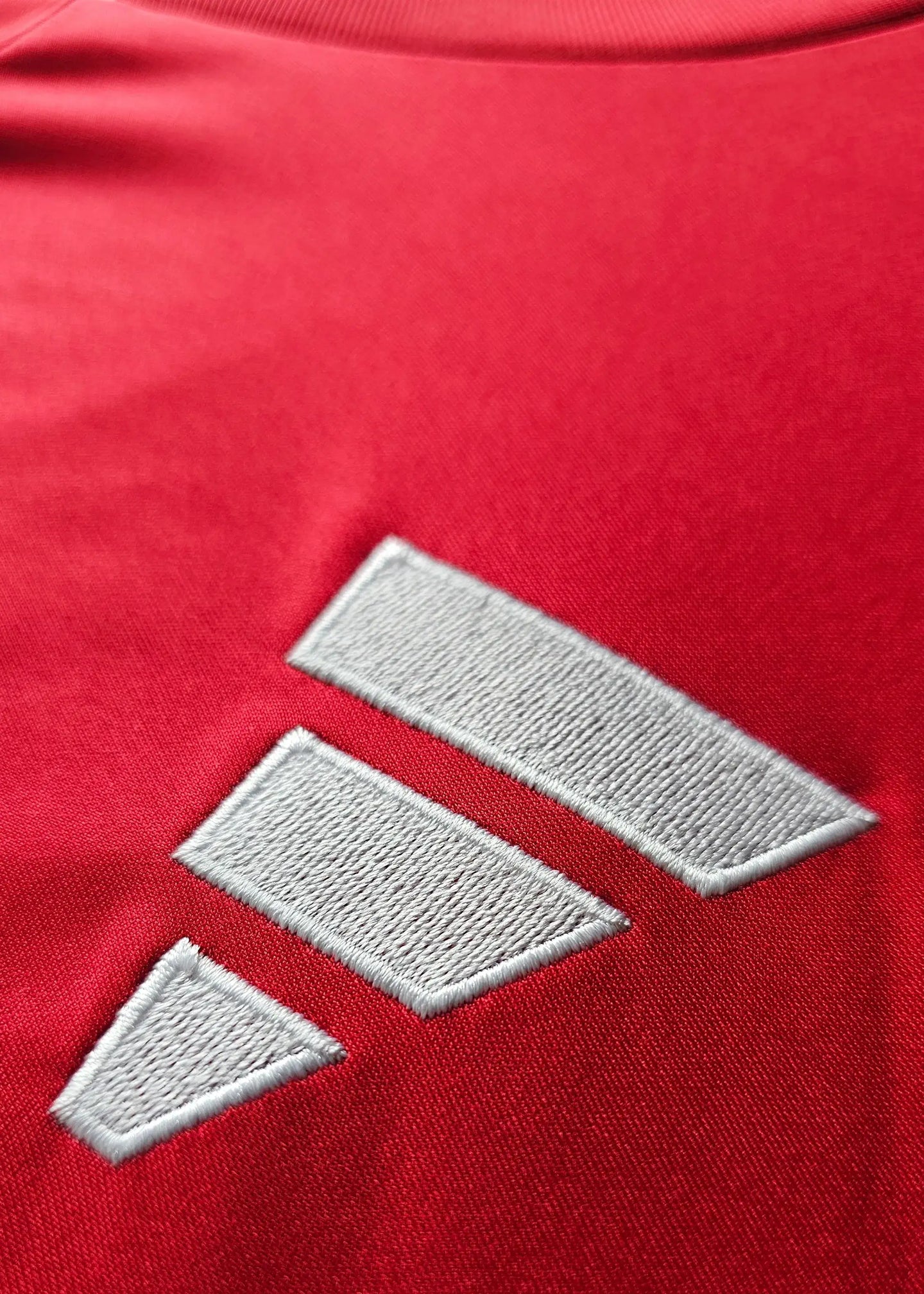 Close-up of Manchester United crest detail in silver on a red football shirt.