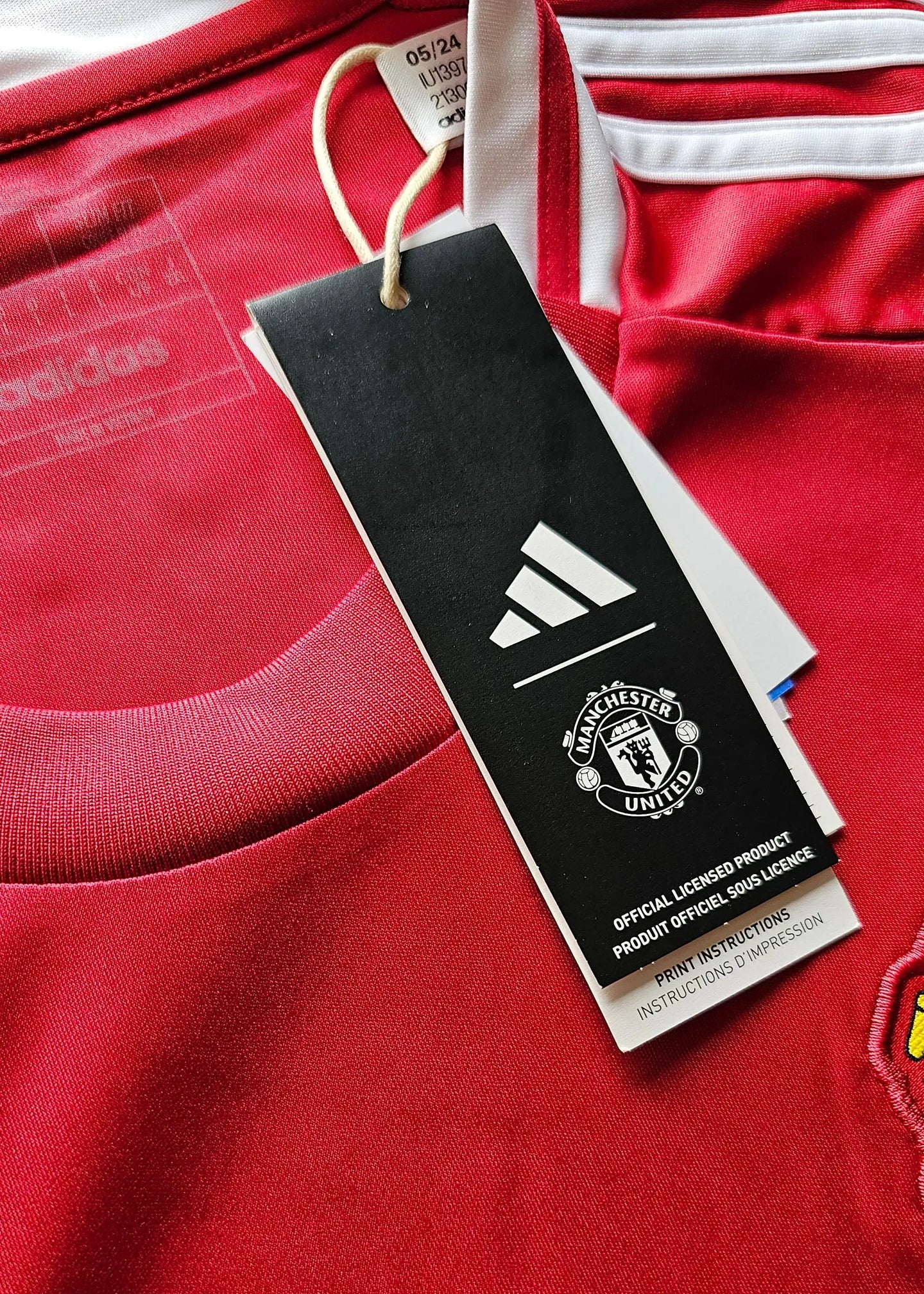 Close-up view showing the adidas tag and Manchester United crest detail on a red football shirt.