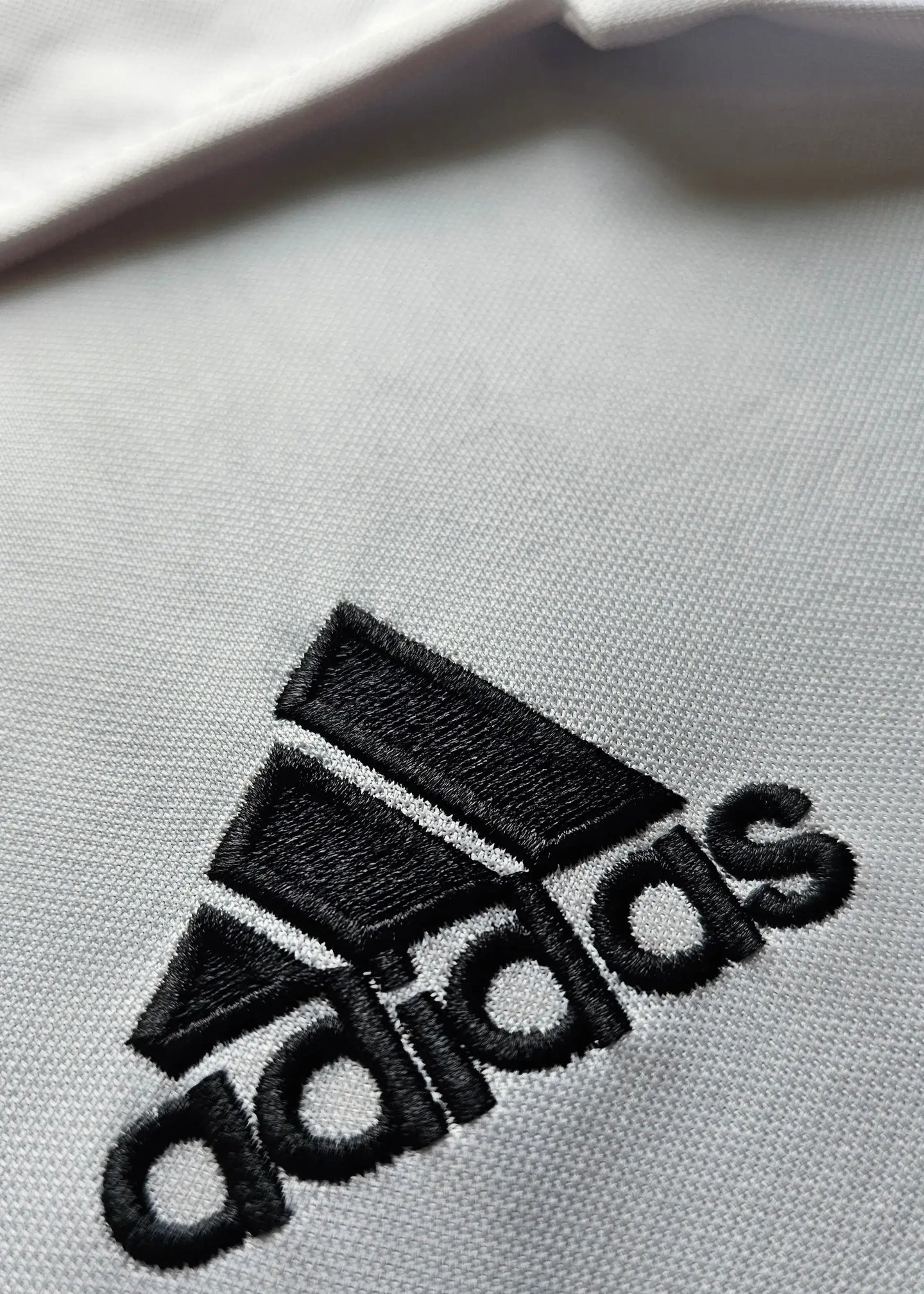 Close-up of the black adidas logo embroidered on a white fabric.