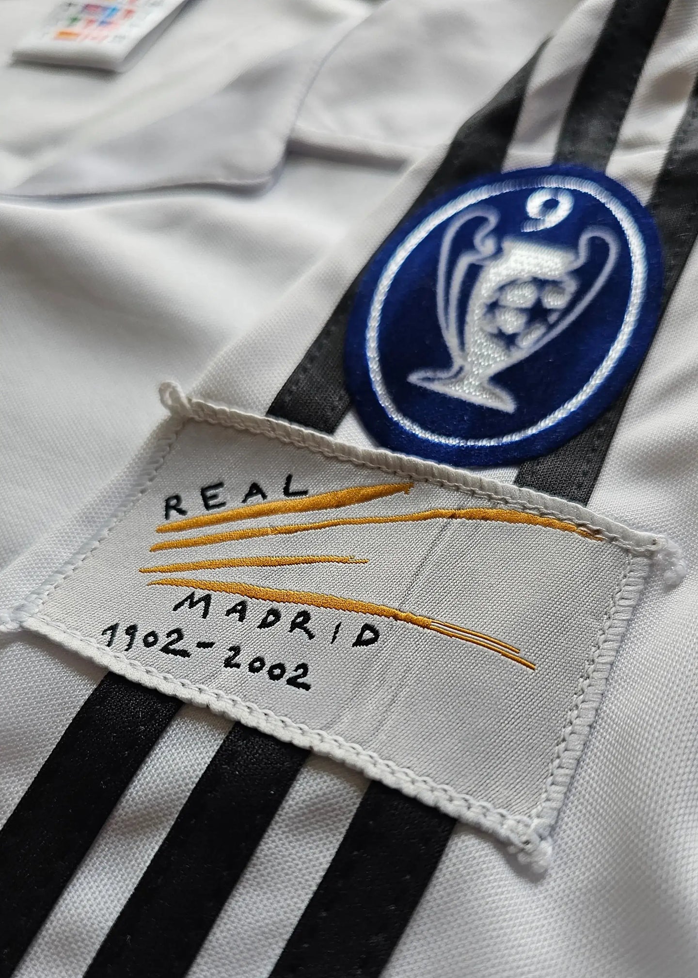 Real Madrid crest and label featuring 'REAL MADRID 1902-2002' detail.