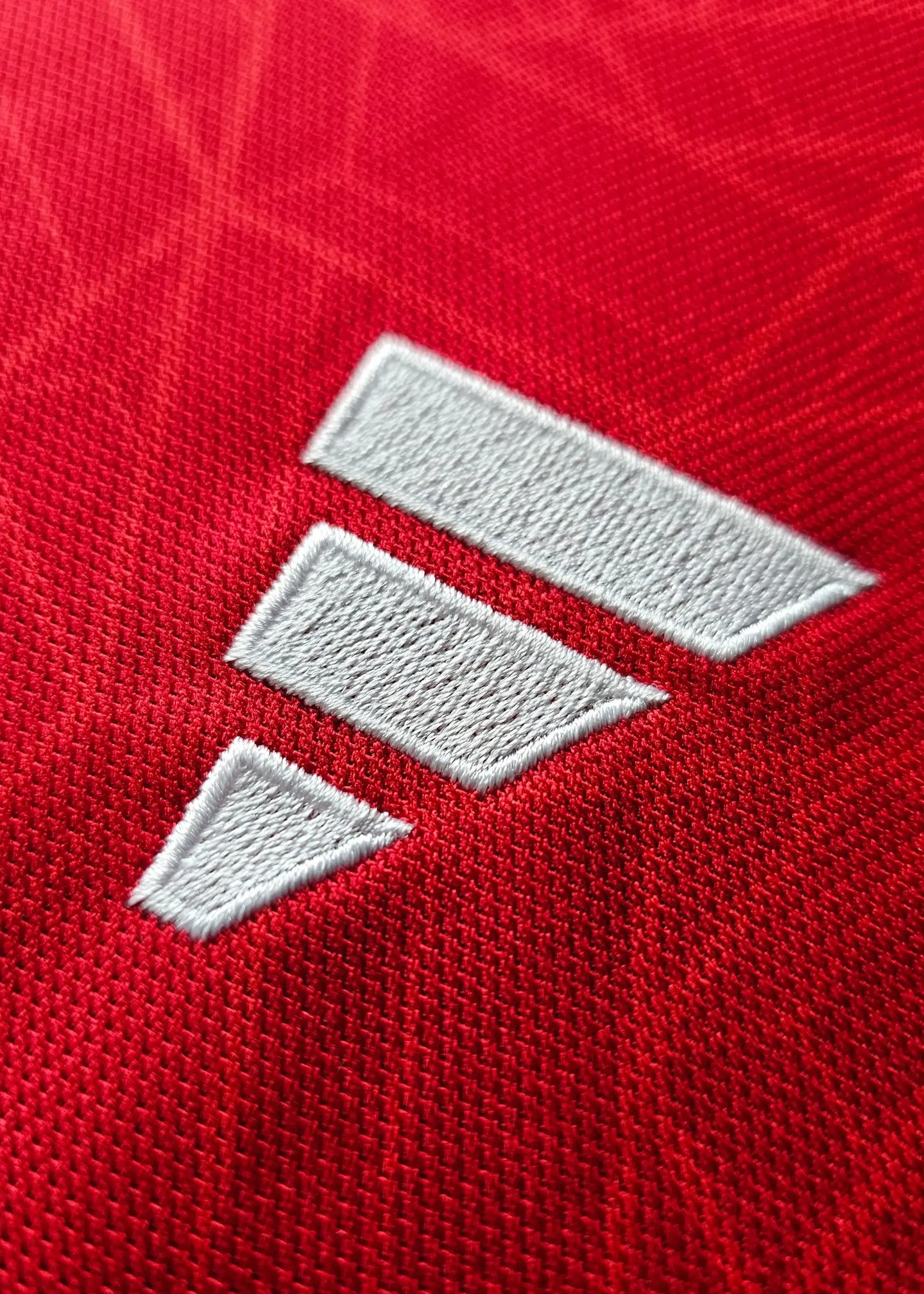 Detail showing the white embroidered brand logo on a red football shirt.
