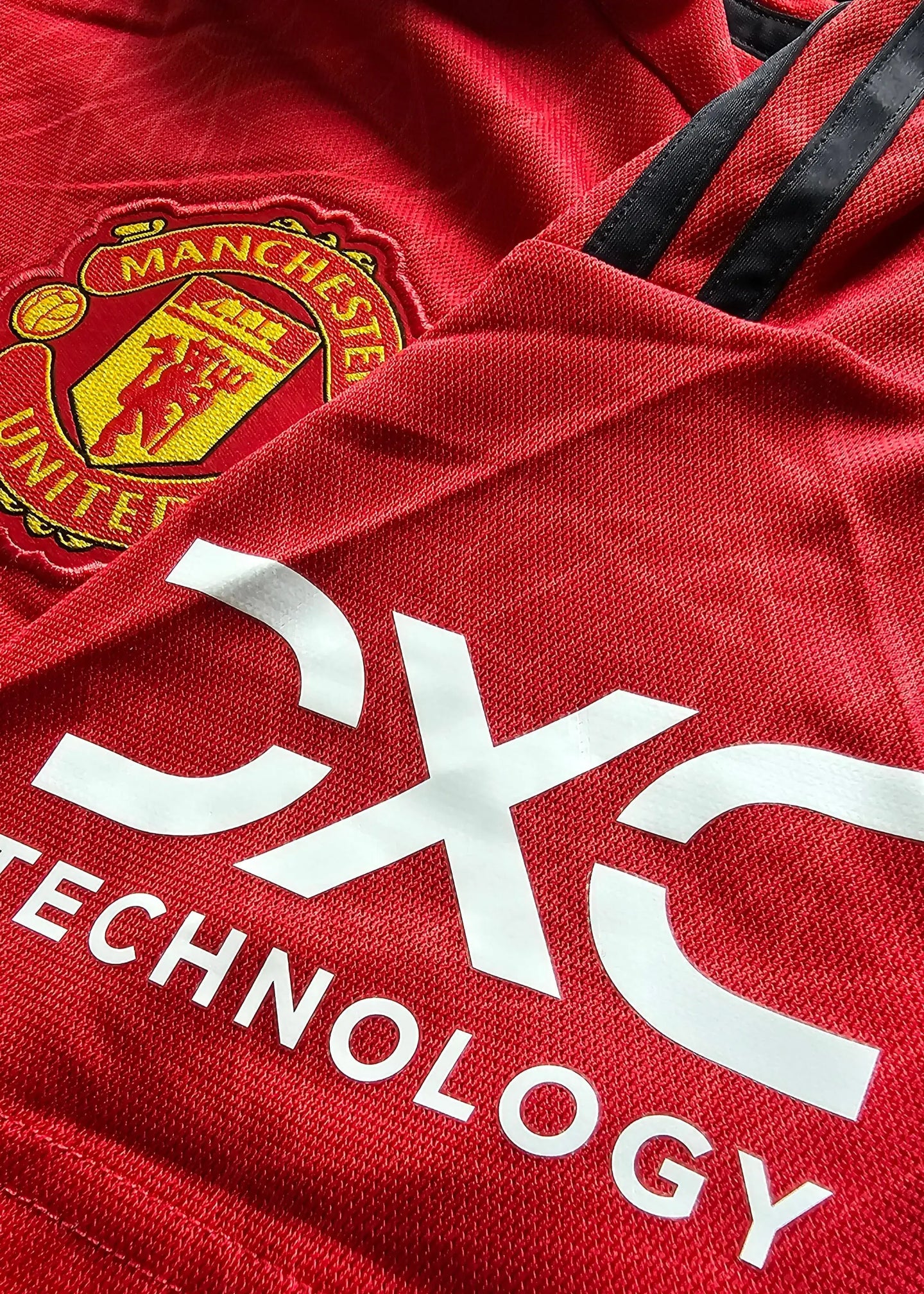 Close-up of Manchester United crest and CX Technology sponsor on red football shirt.