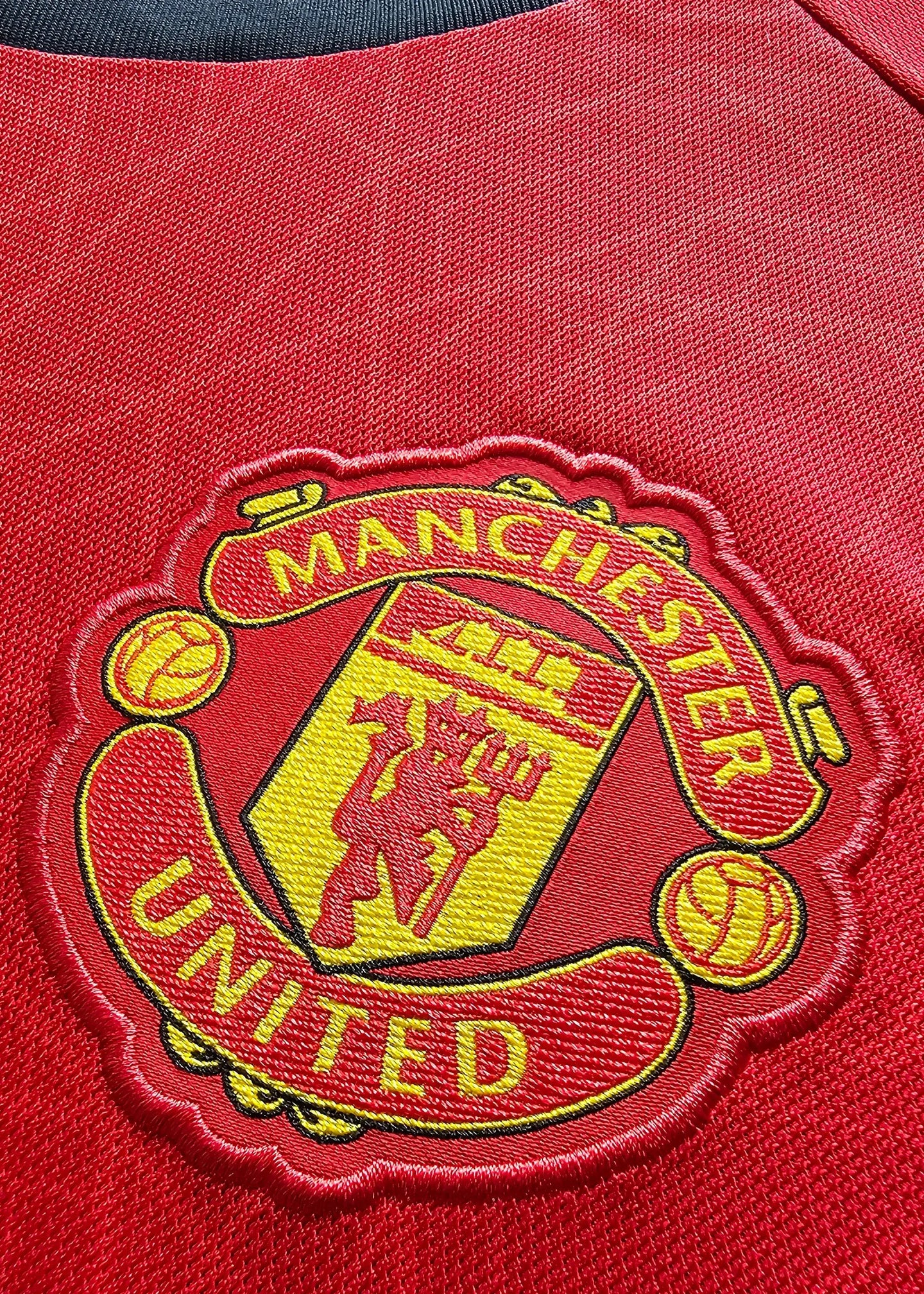 Close-up of Manchester United crest with text 'MANCHESTER' and 'UNITED' in yellow on red fabric.