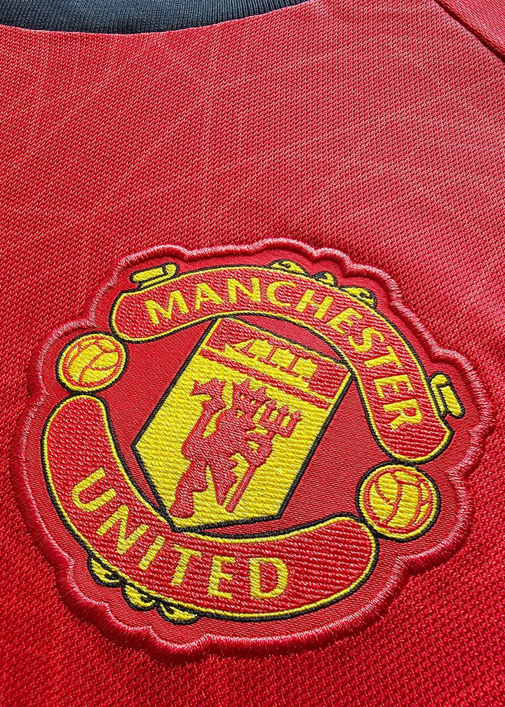 Close-up of Manchester United crest with text 'MANCHESTER' and 'UNITED' in yellow on red fabric.