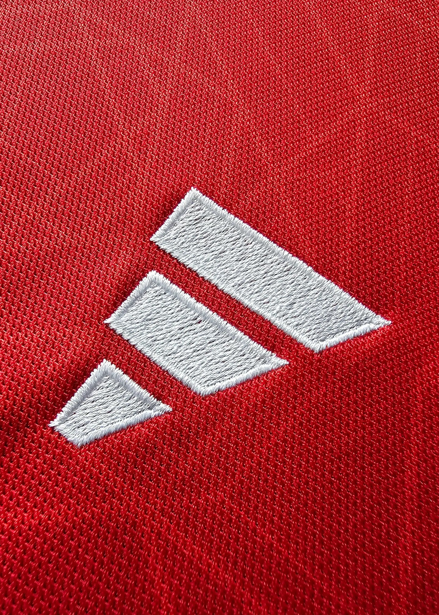Close-up of white adidas logo on red fabric of soccer jersey.