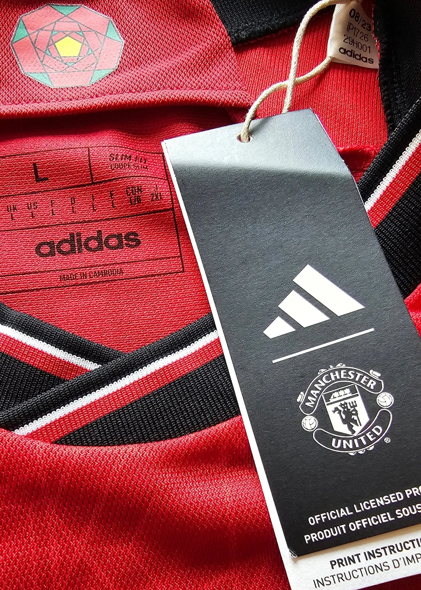 Crest detail featuring Manchester United emblem, adidas logo, and size L label on red soccer jersey.