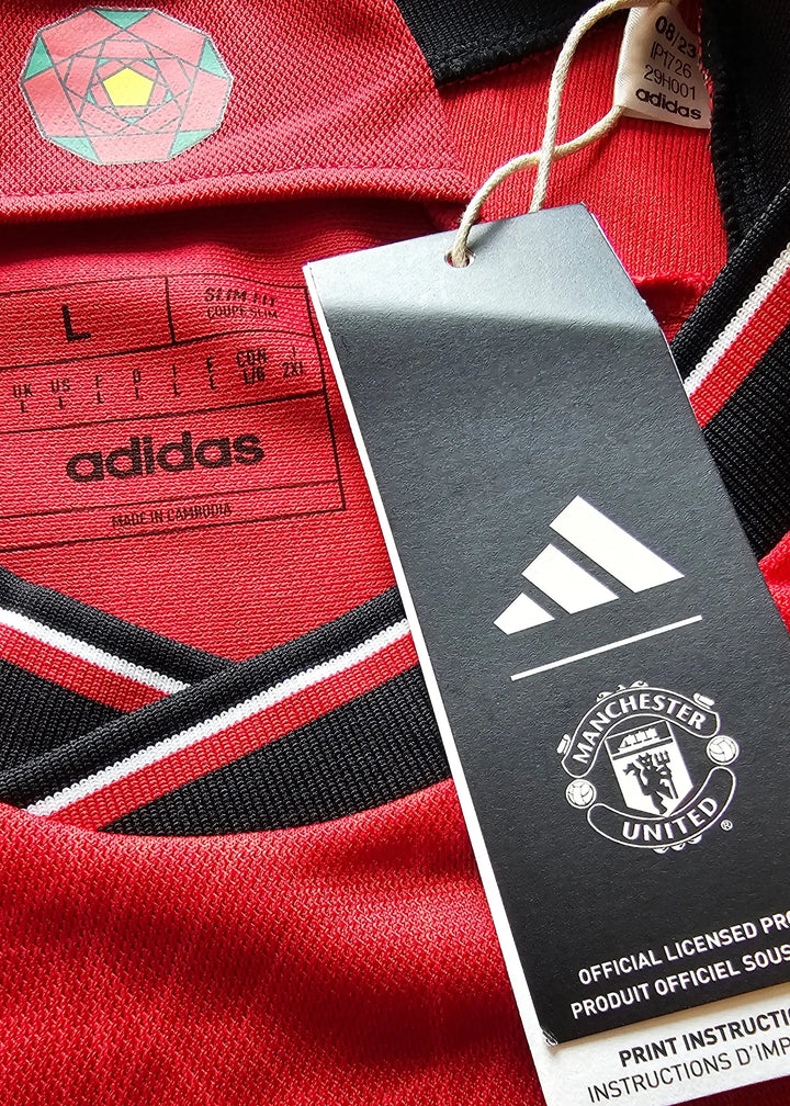 Crest detail featuring Manchester United emblem, adidas logo, and size L label on red football shirt.