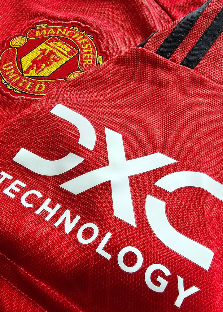 Close-up showing Manchester United crest and CX Technology sponsor on red football shirt.