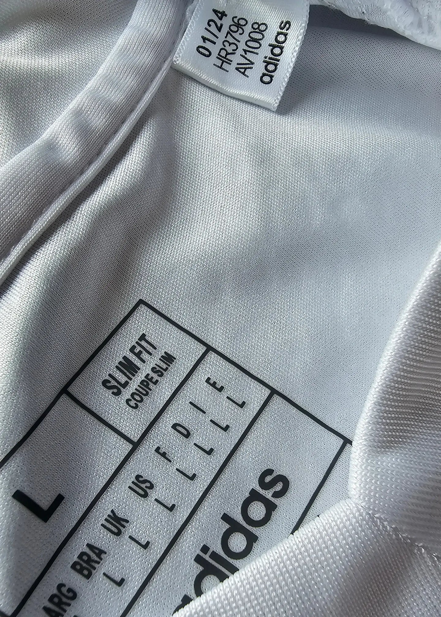 Size L label detailing 'SLIM FIT' and 'adidas' branding on white fabric.