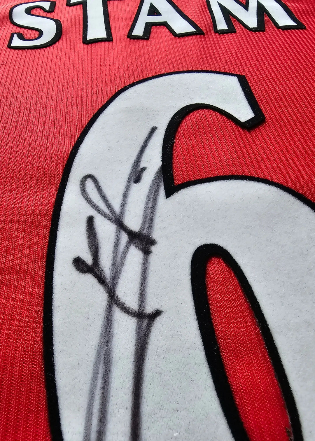 Detail view showing the signature of Stam over the No. 6 on a red football shirt.