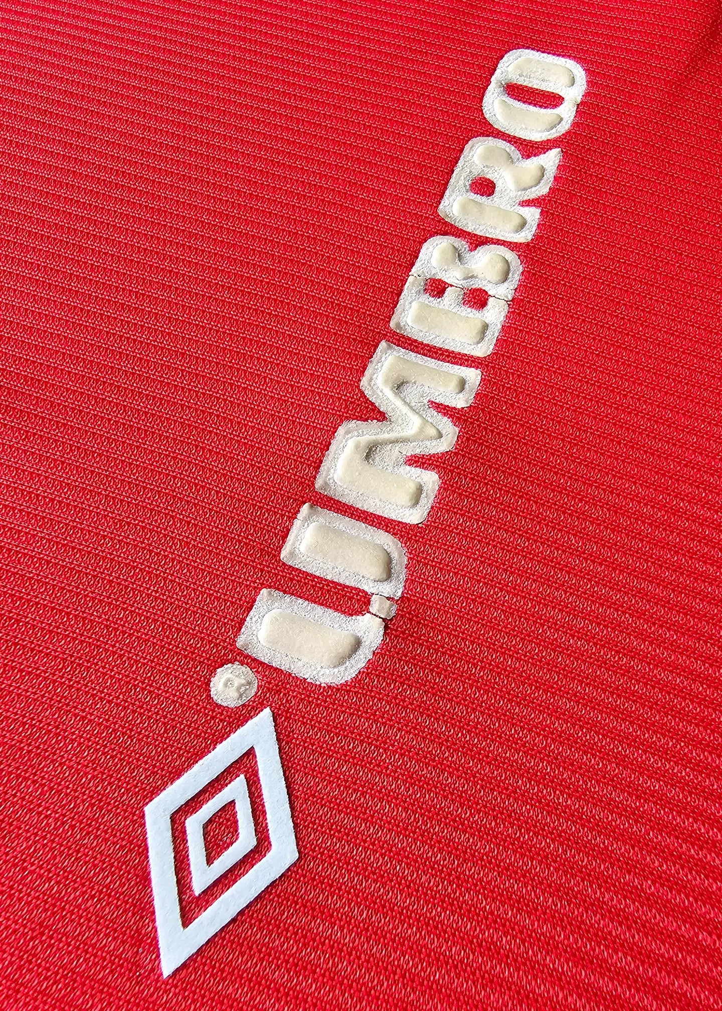 Detail showing white Umbro logo on a red Manchester United football shirt.