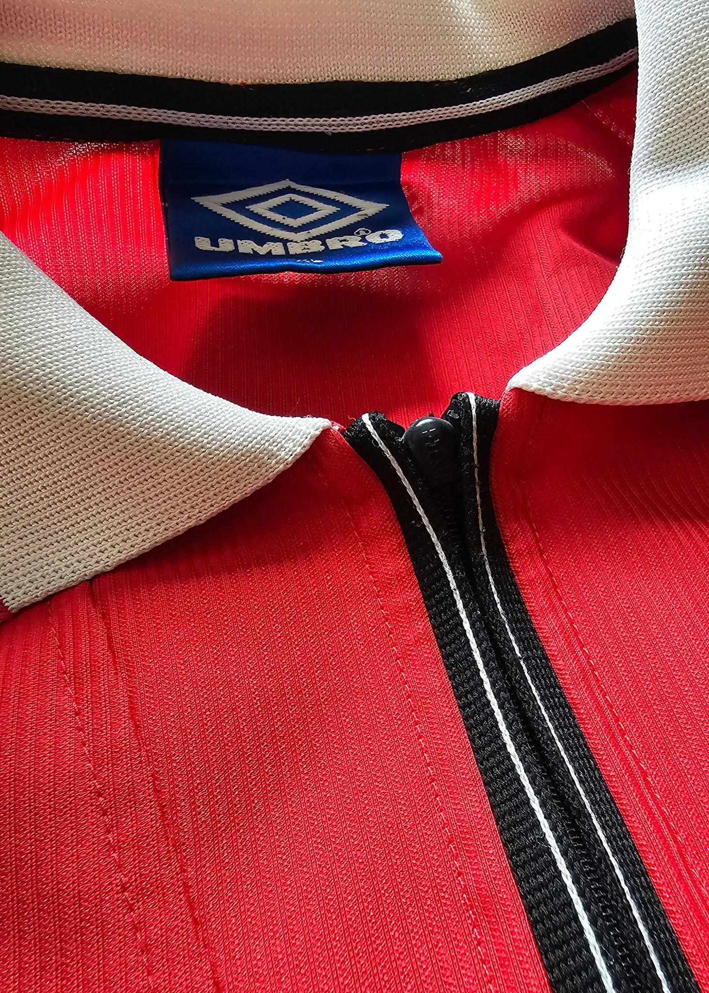 Close-up showing red fabric, collar details, and Umbro brand tag on football shirt.