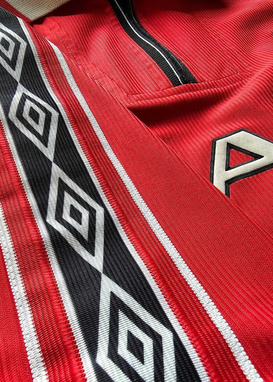 Close-up of red football shirt featuring black and white diamond pattern detailing.