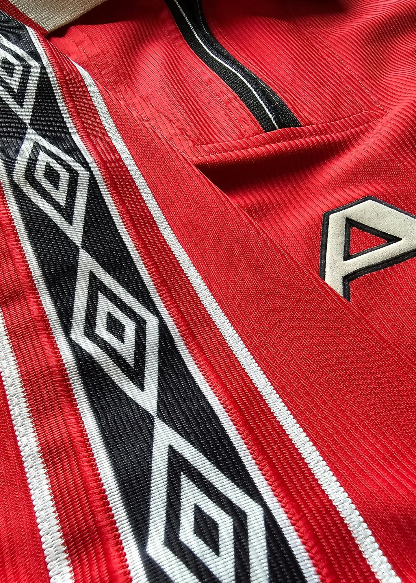 Close-up detail of red football shirt featuring black and white diamond pattern and collar.