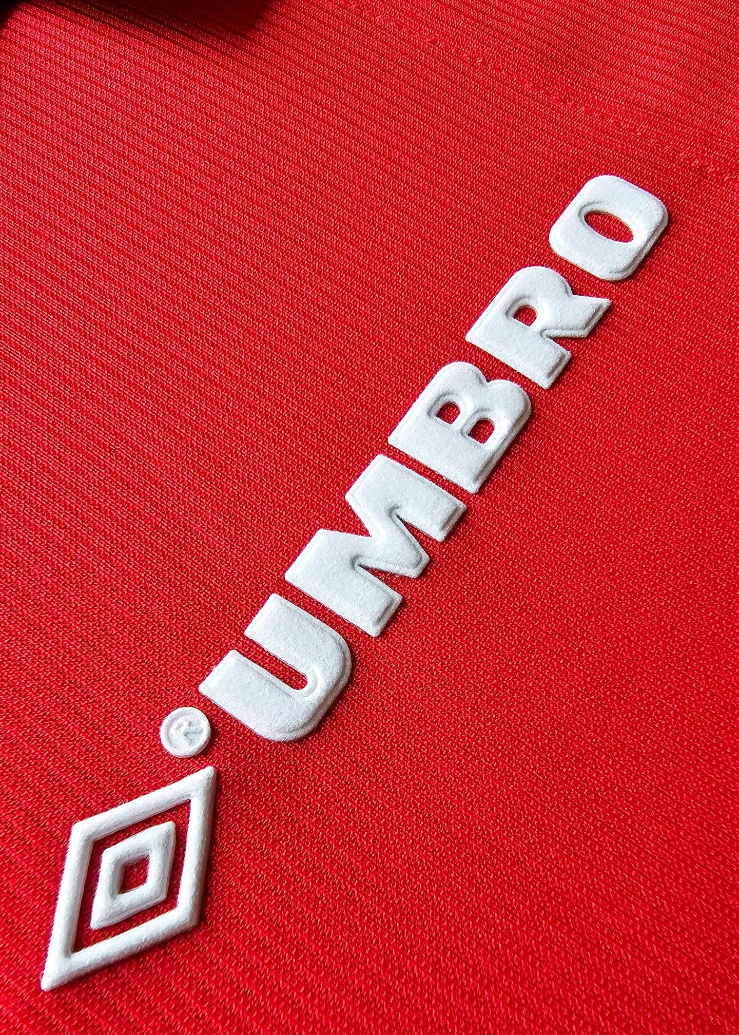 Close-up view of the white Umbro logo stitched onto a red soccer jersey.