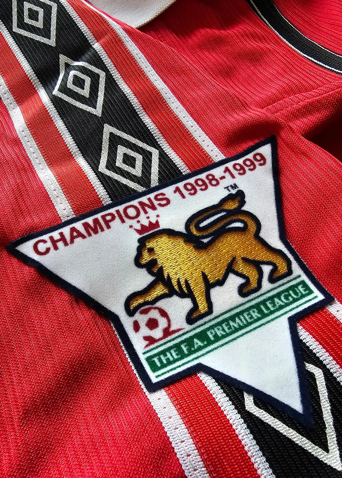 Crest detail featuring 'CHAMPIONS 1998-1999' and lion logo from Manchester United F.C.