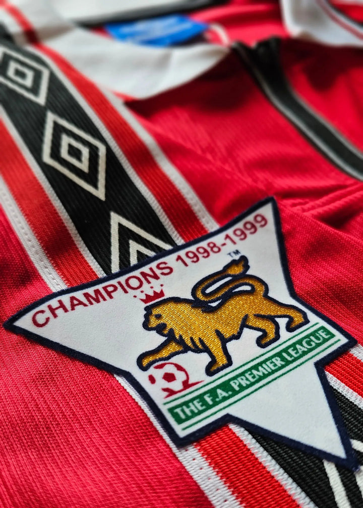 Detail view of Manchester United crest featuring 'CHAMPIONS 1998-99' and lion emblem.