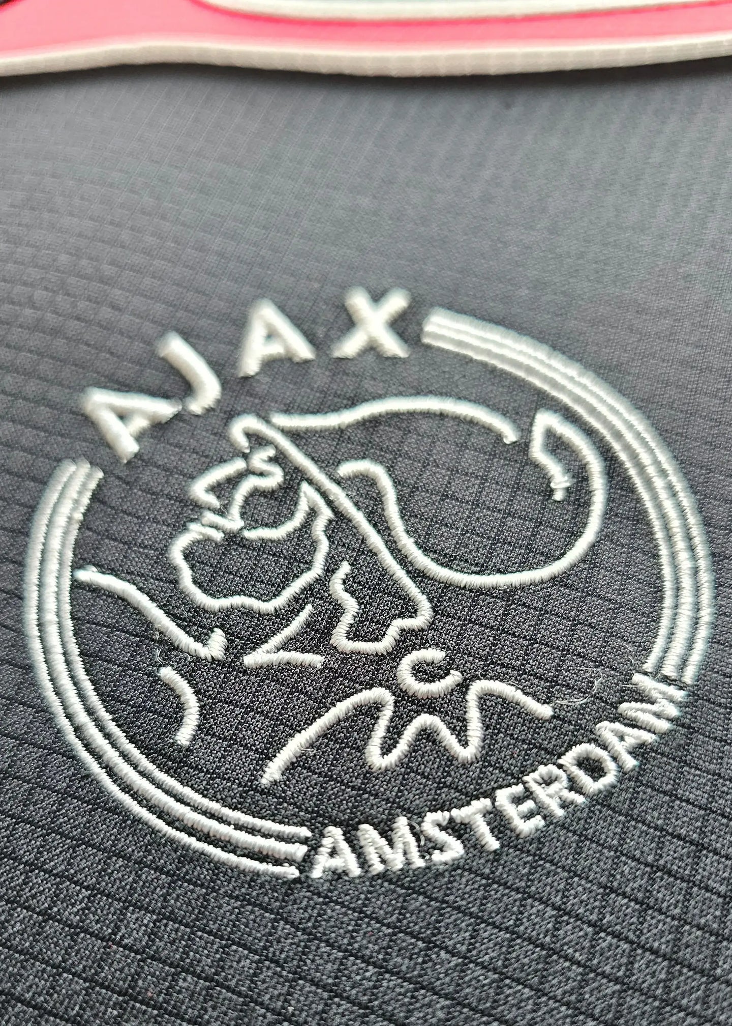 Crest detail featuring the Ajax emblem with Amsterdam lettering in white stitching.