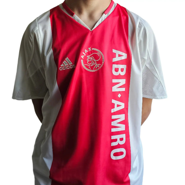 Front view of the red-and-white Ajax shirt with the Ajax crest, adidas logo, and 'ABN AMRO' sponsor text.