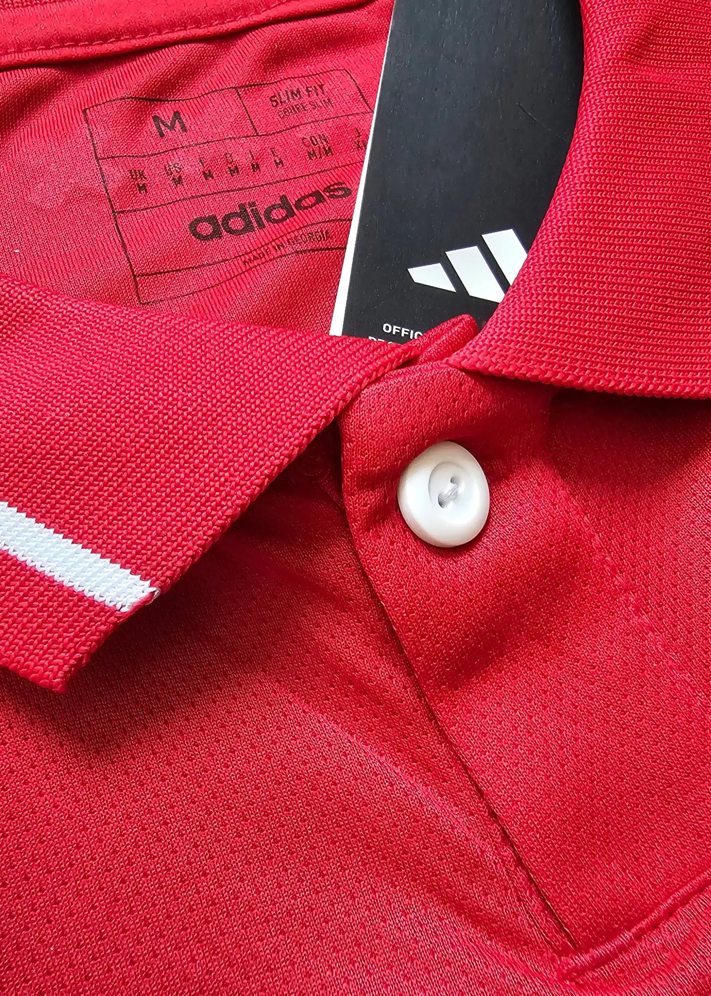 Close-up of red shirt collar with white stripes and adidas tag, size M, official label visible.