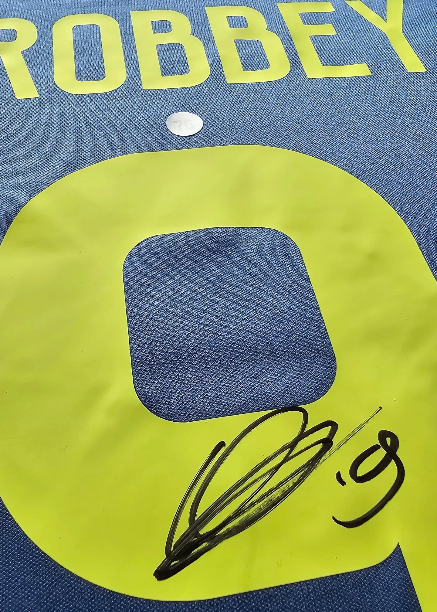 Detail showing signature on No. 9 jersey with "BROBBEY" printed above in yellow on blue fabric.