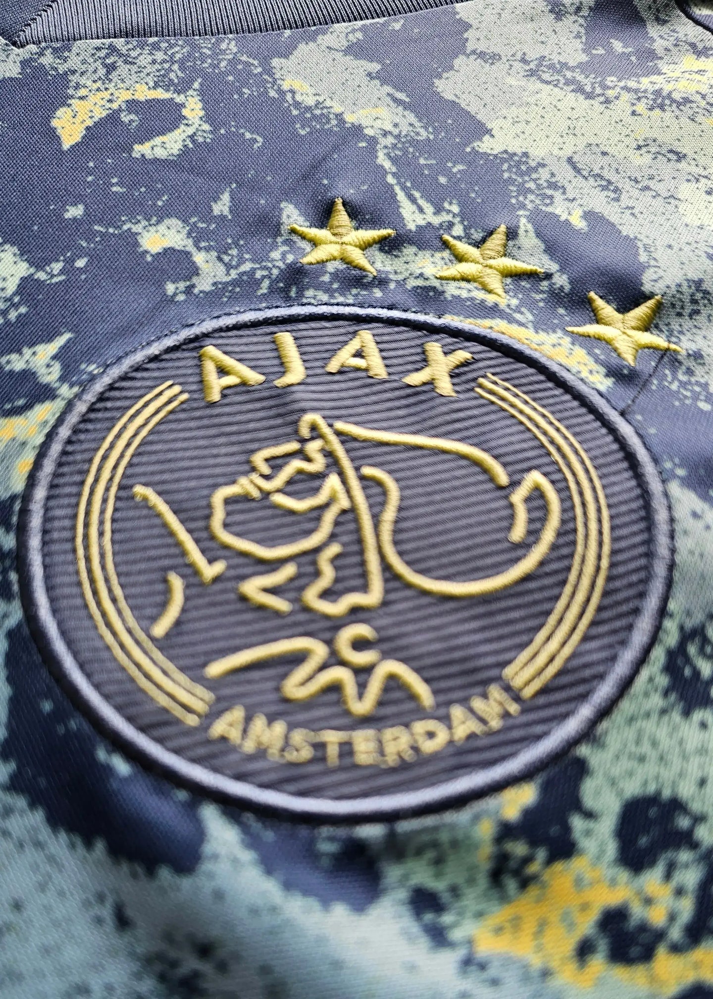 Crest detail featuring Ajax logo and three stars on a blue and yellow background.