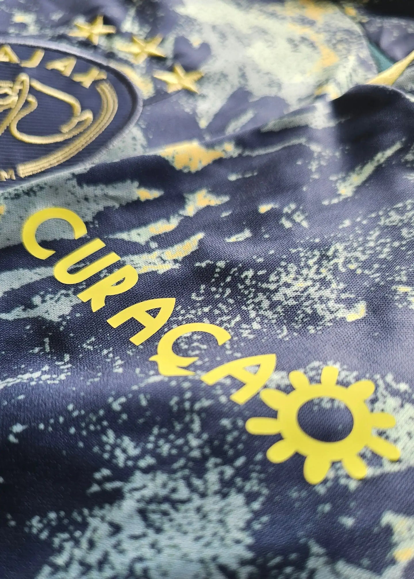 Close-up showing AFC Ajax crest, three stars, and 'CURACAO' in yellow lettering.