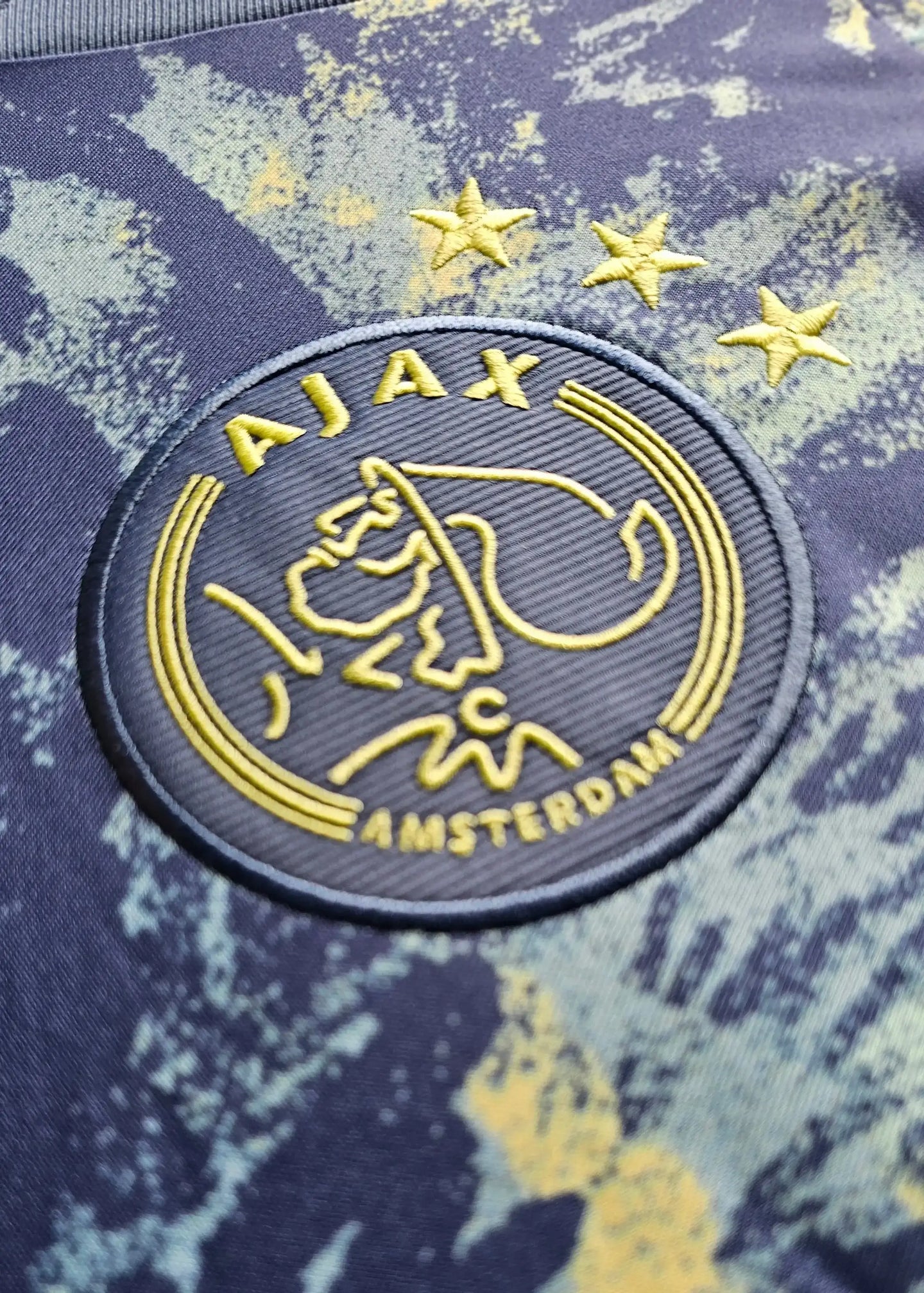 Ajax crest with three stars and signature detail visible on blue and yellow design.