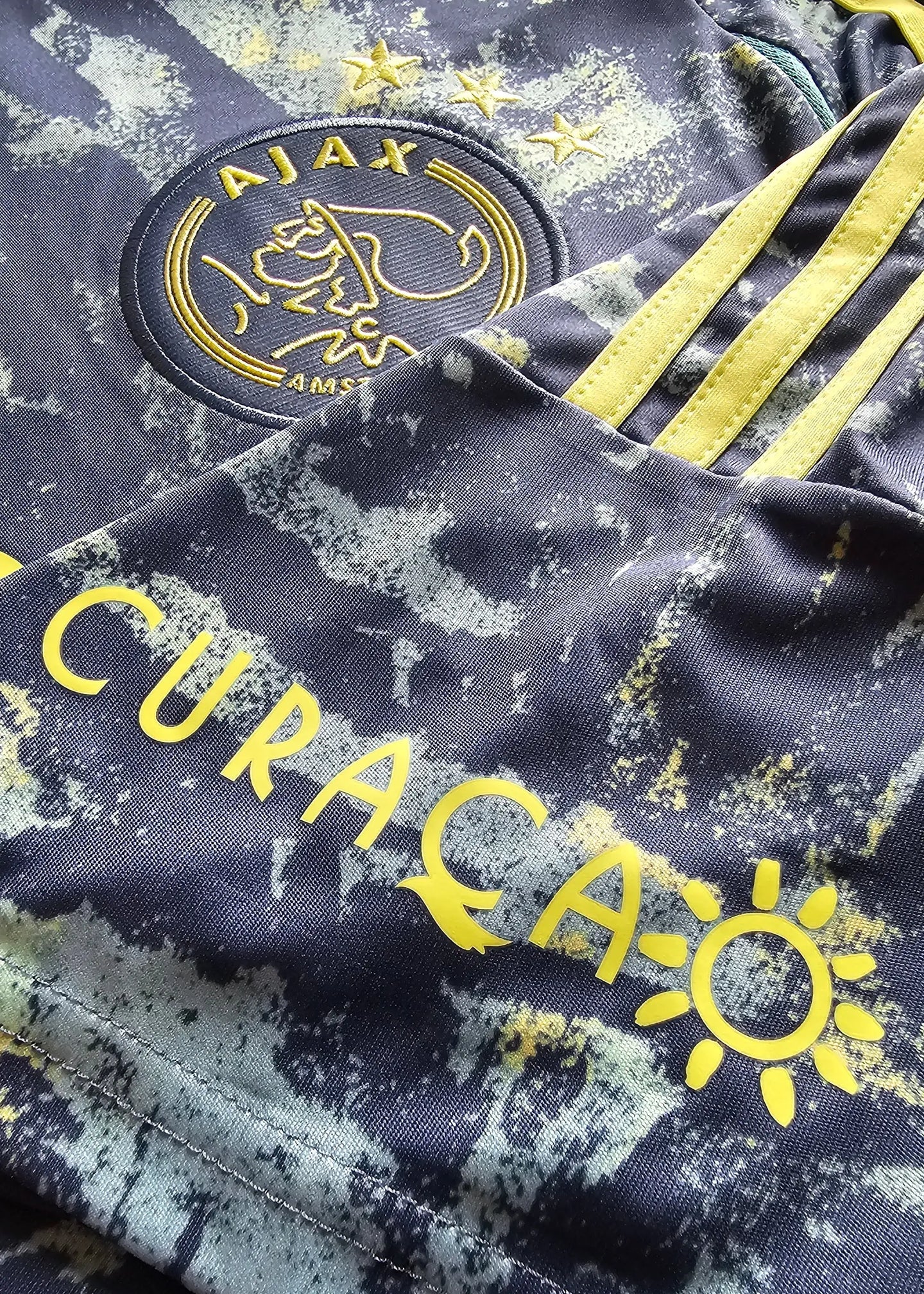Crest detail featuring AJAX and three stars above in yellow on a navy blue shirt, with CURAÇAO text.