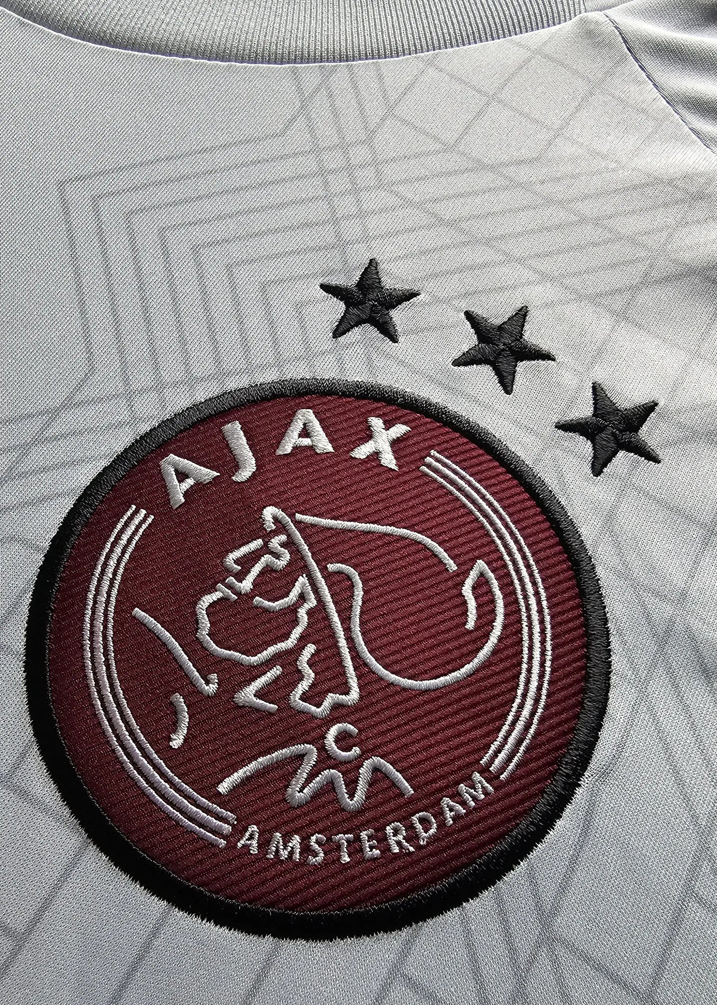 Crest detail showing AJAX with three stars above and Amsterdam in white embroidery.