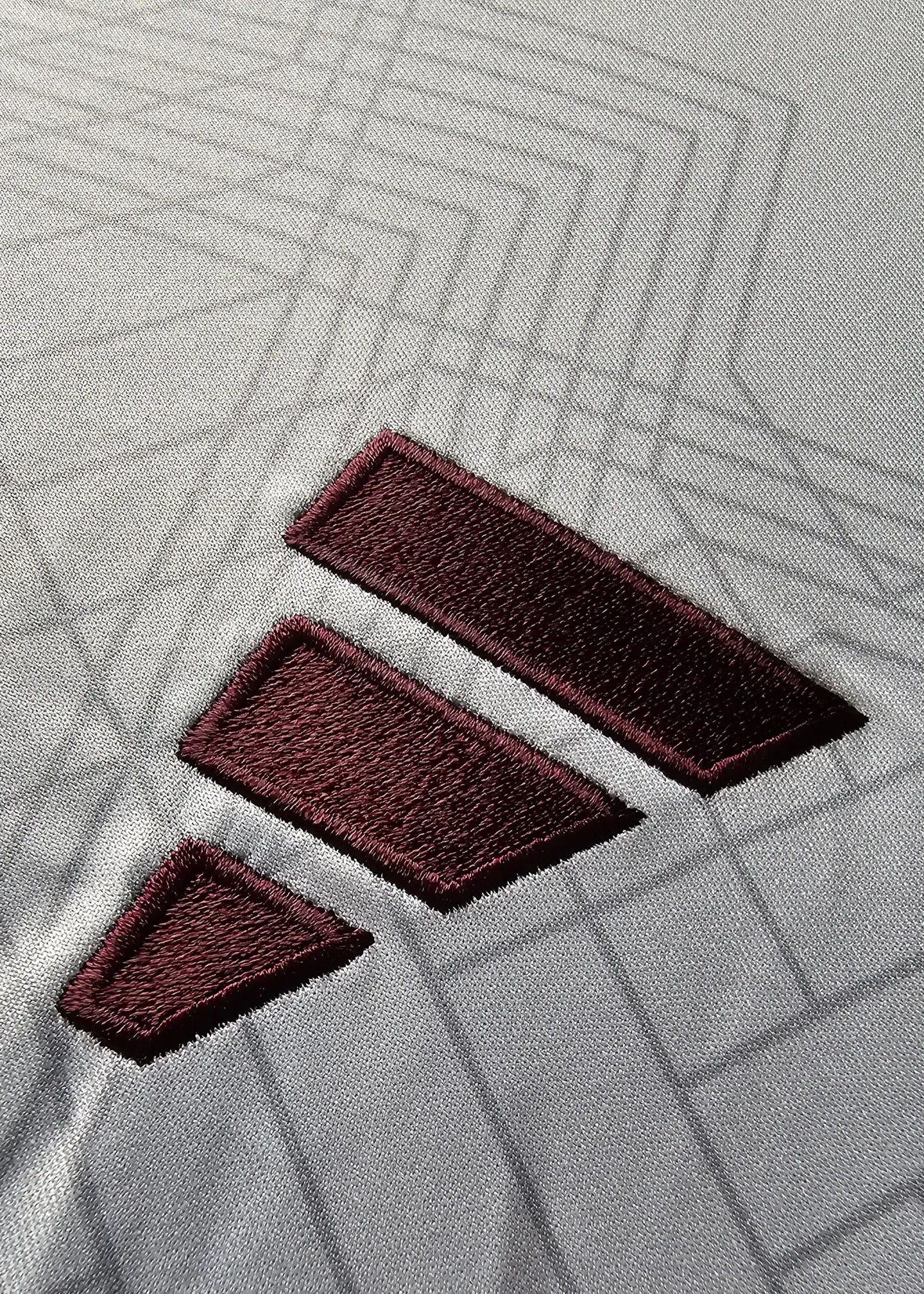 Detailed view of the adidas logo in maroon on a gray background, showing embroidered texture.