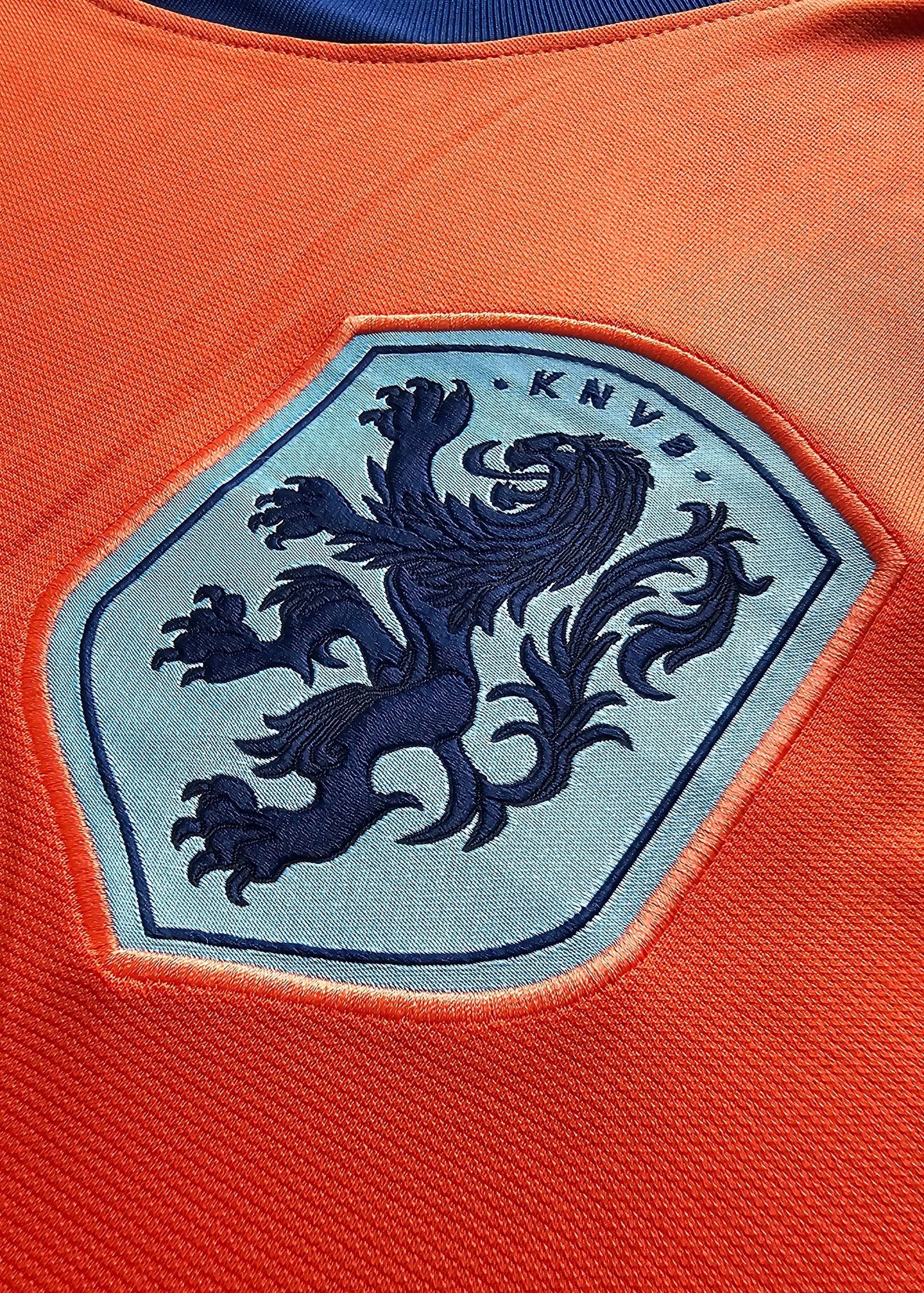 Close-up of the Holland crest featuring a lion and the letters KNVB in blue on an orange football shirt.