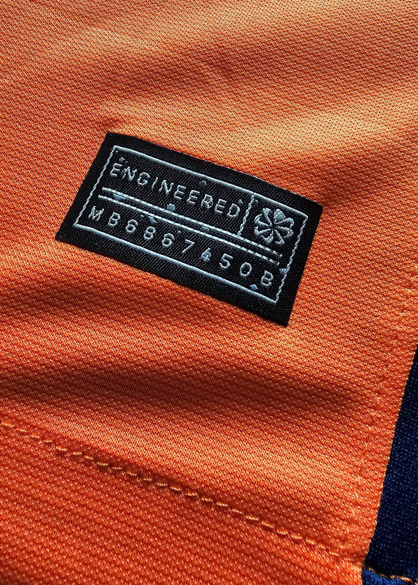 Black label with text 'ENGINEERED' and code 'MB6867450B' on orange fabric.