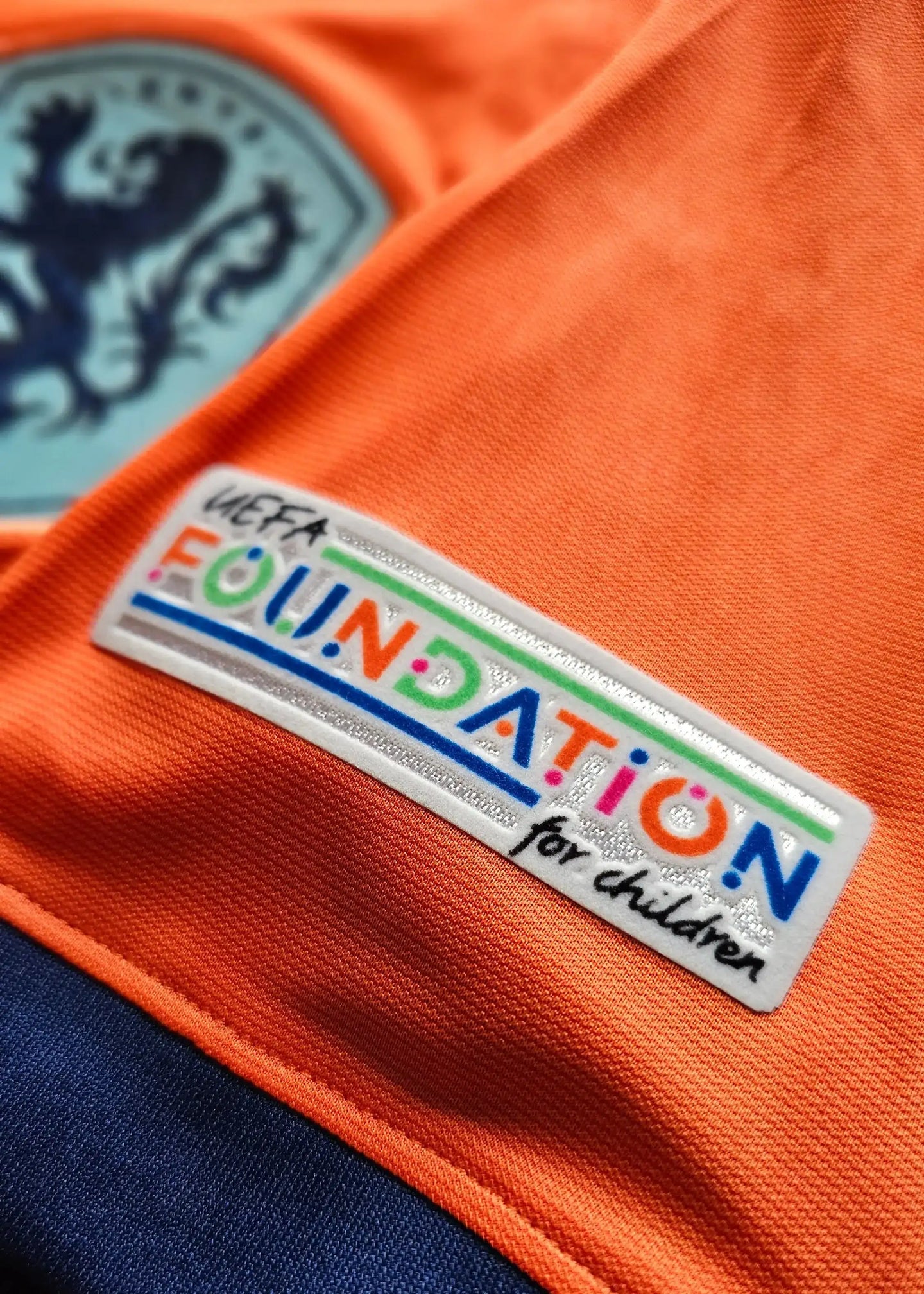 Detail showing UEFA FOUNDATION for children patch on orange fabric with crest.