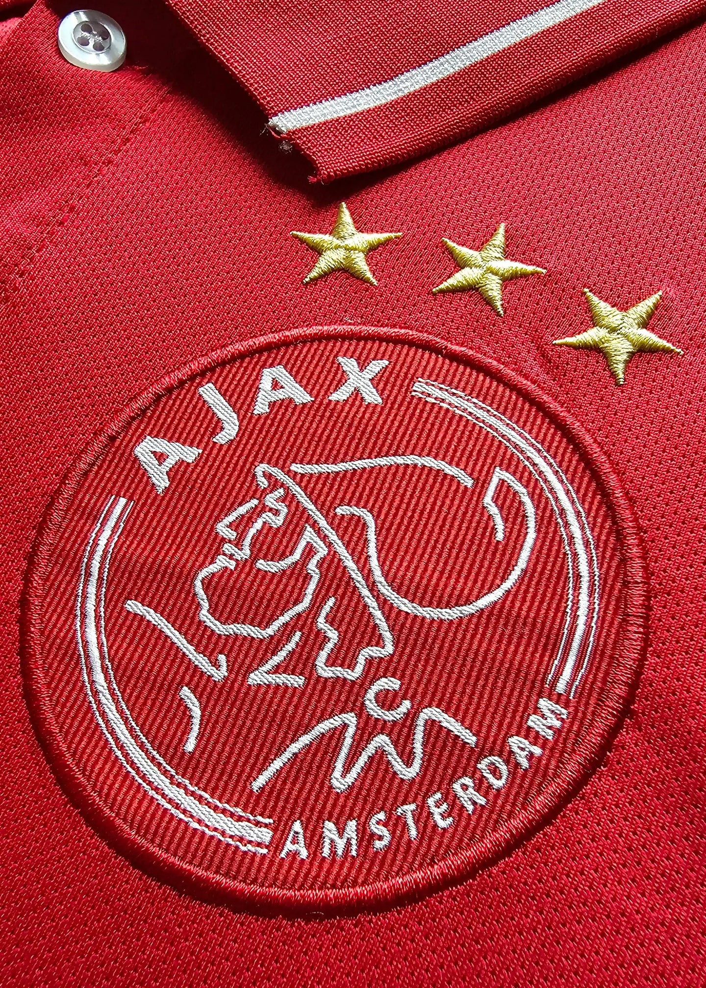 Close-up of Ajax crest with three stars on a red background.