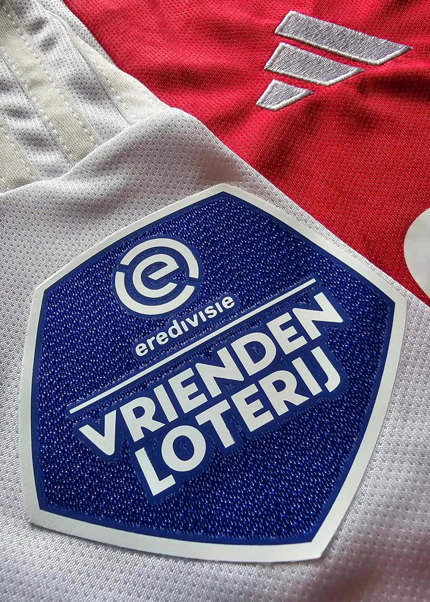 Detail view of the VRIENDEN LOTERIJ logo and eredivisie branding on a red and white football shirt.