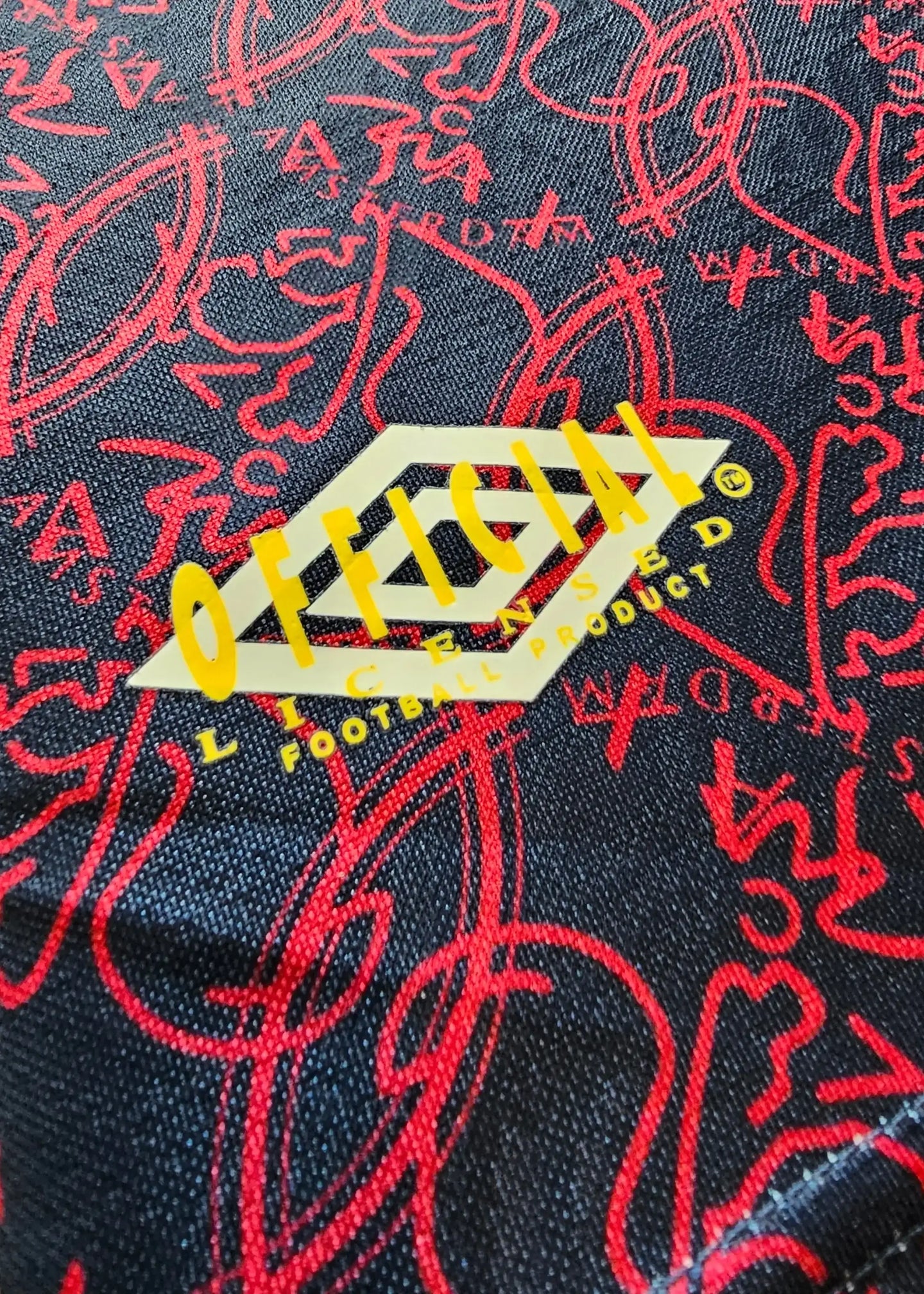 Detail view showcasing the OFFICIAL licensed football product logo in yellow on a patterned black background.