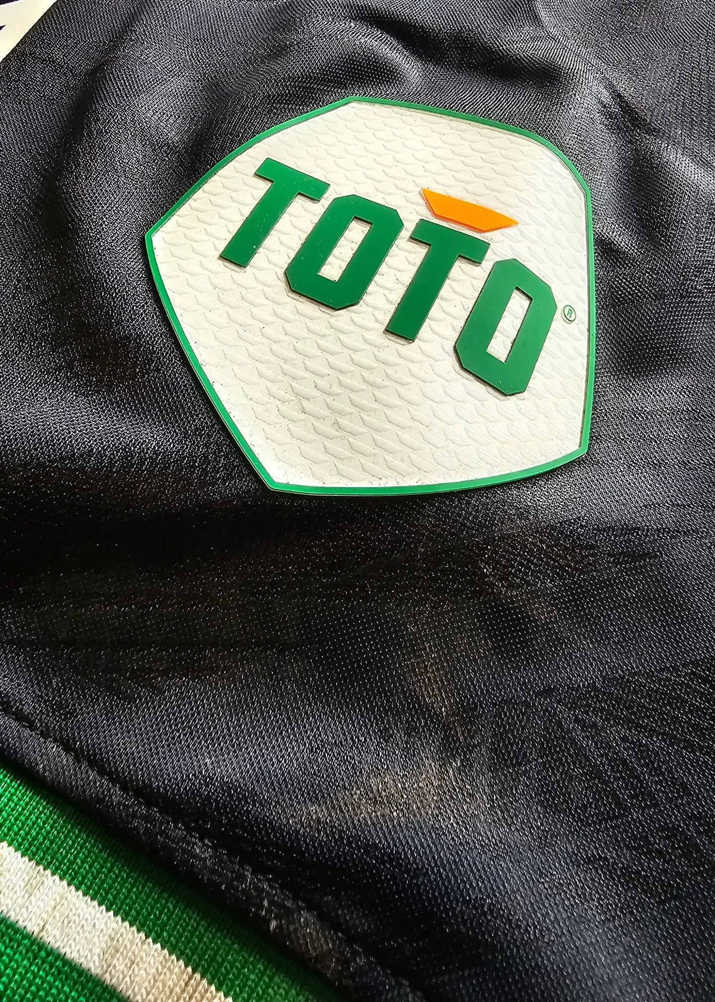 Crest detail featuring TOTO logo on a black background with green accents.