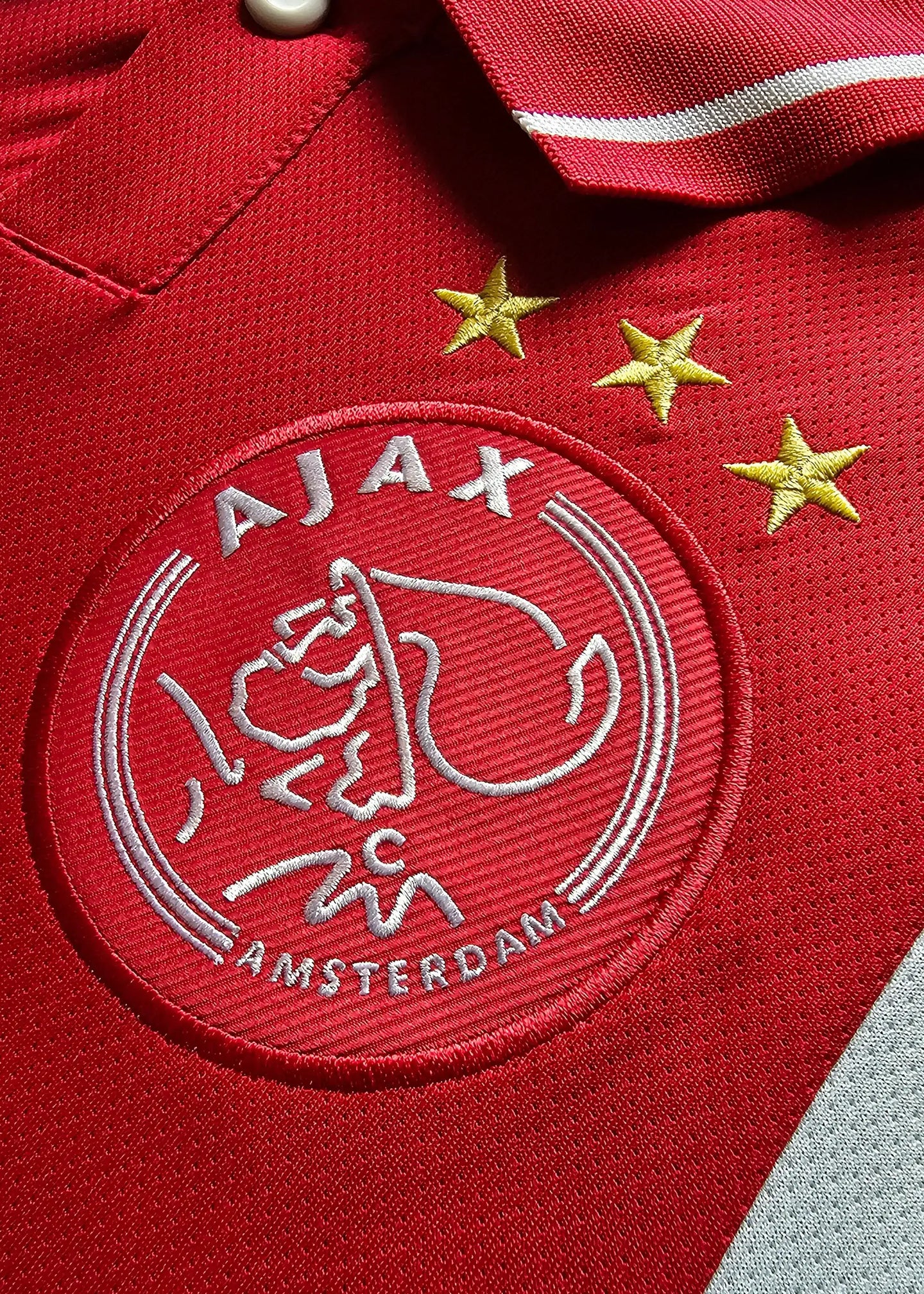 Crest detail showing Ajax logo with three stars in red and white colors.