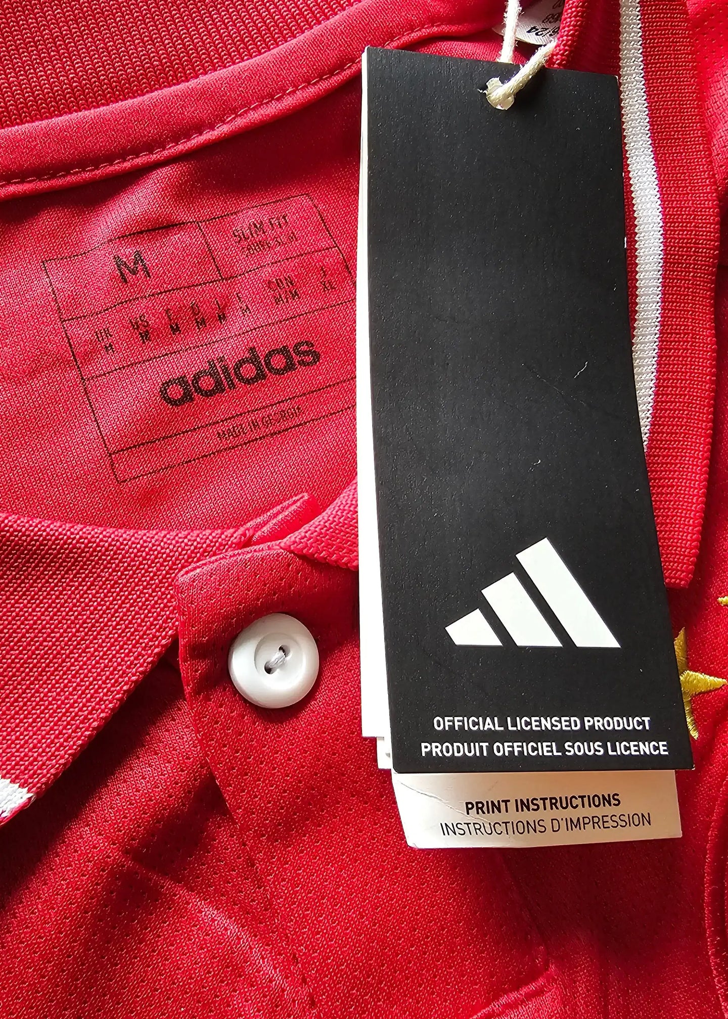 Close-up of the Adidas tag and size label on a red Ajax football shirt with white accents.