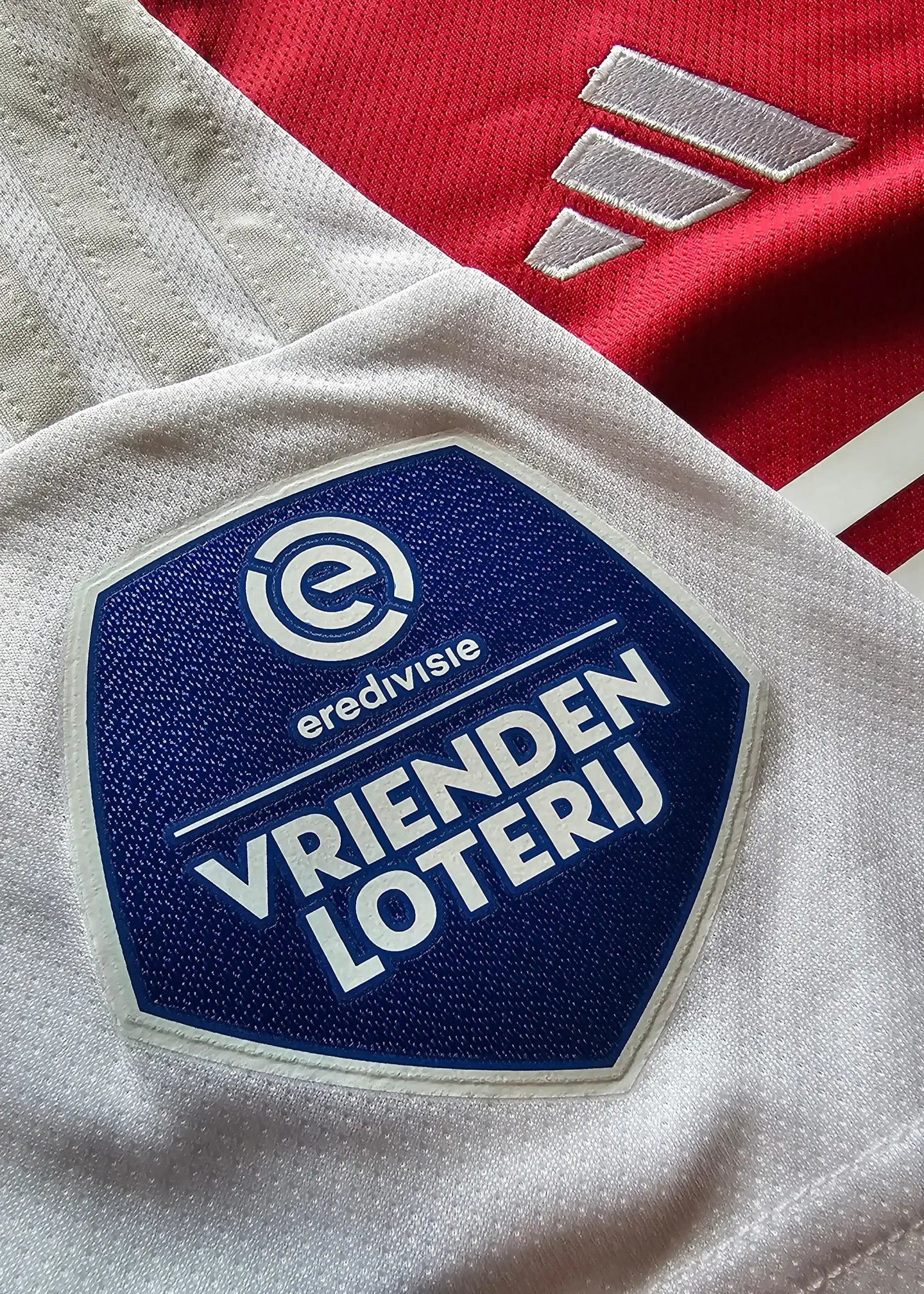 Crest detail showing Vandiensten Loterij and eredivisie logos on white section of Ajax shirt.