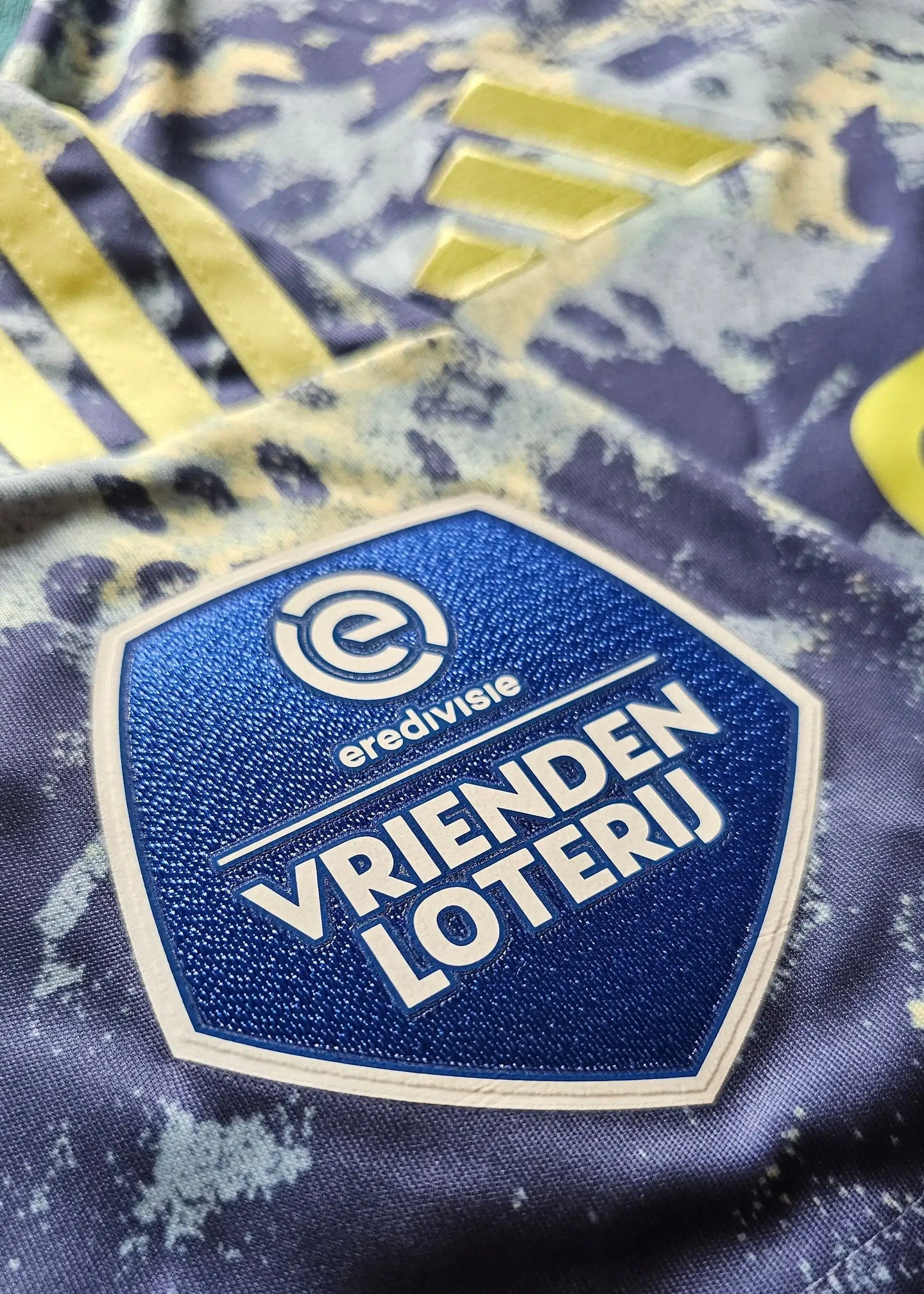 Detail view of the AFC Ajax crest featuring 'VRIENDEN LOTERIJ' on a blue and yellow football shirt.
